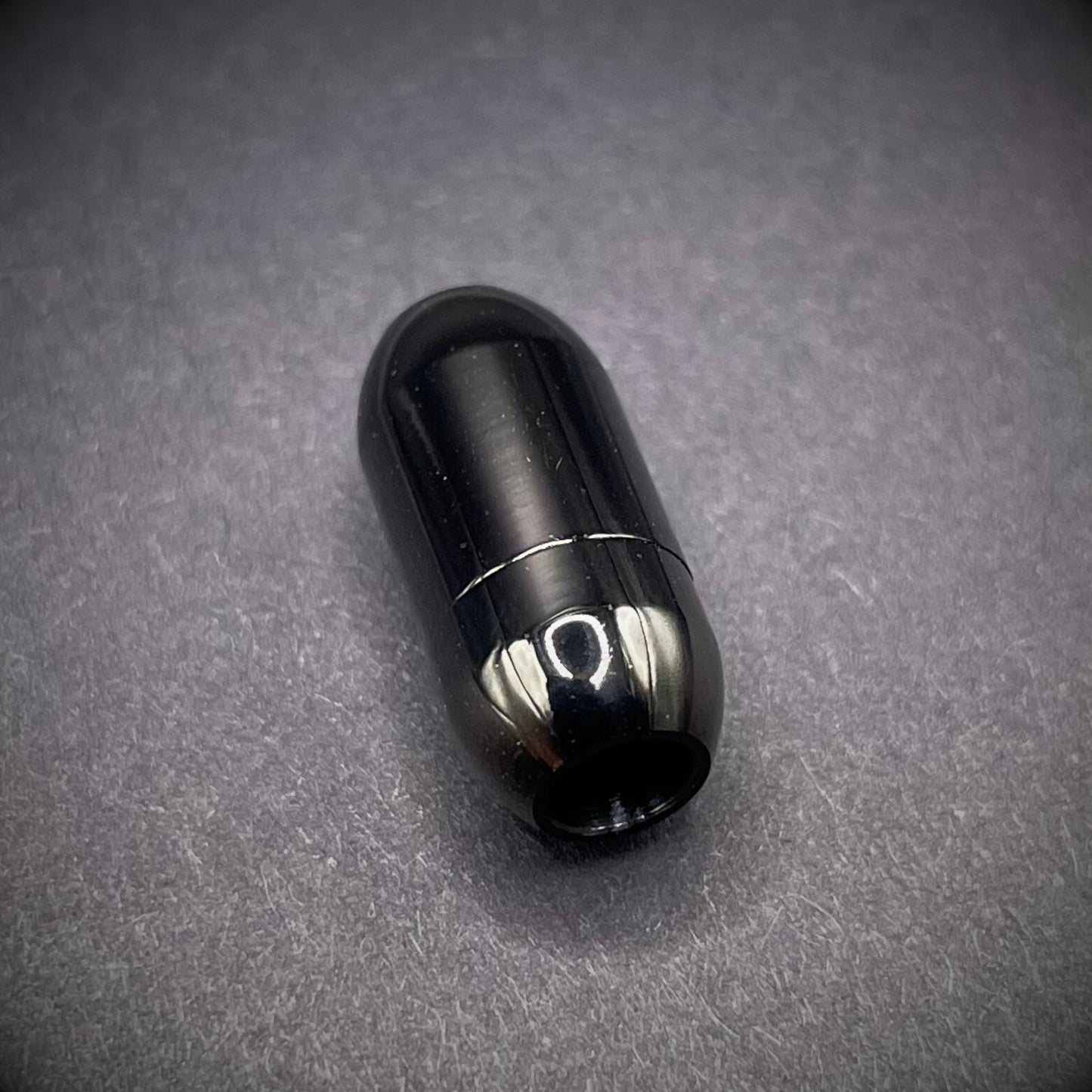Black cylindrical metal magnetic bracelet clasp, displayed on a dark textured background.