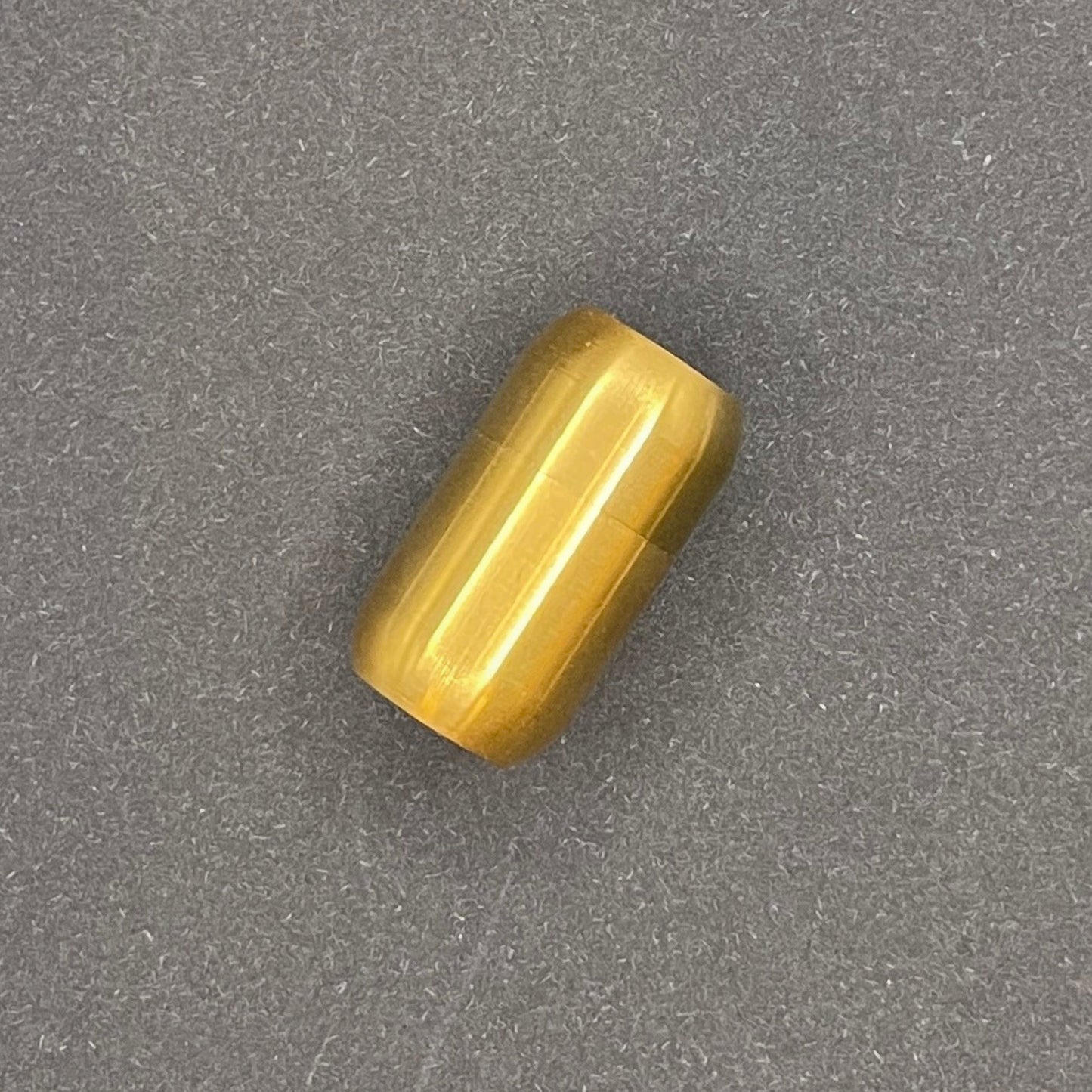 Gold cylindrical metal magnetic bracelet clasp, displayed on a dark textured background.