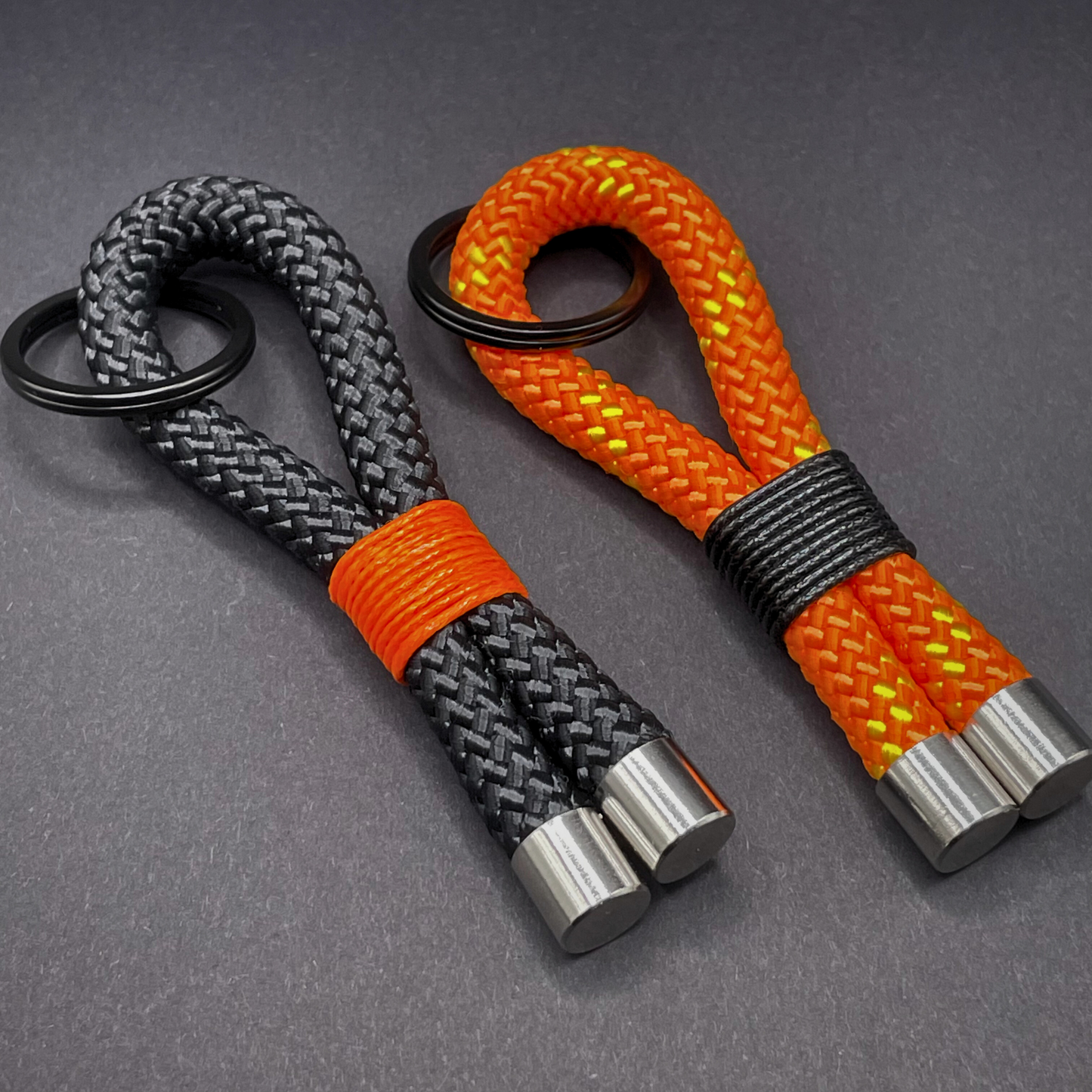 Flat lay of black braided rope keychain with silver end caps and orange whipping on a dark background.