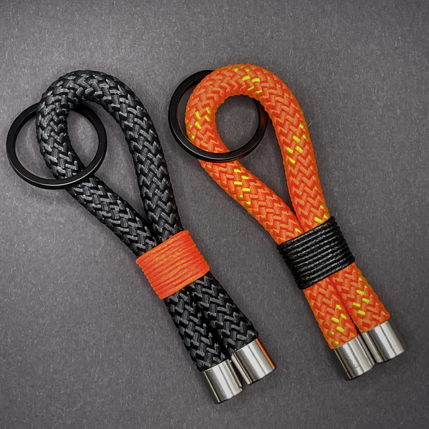 Flat lay of black braided rope keychain with silver end caps and orange whipping on a dark background.