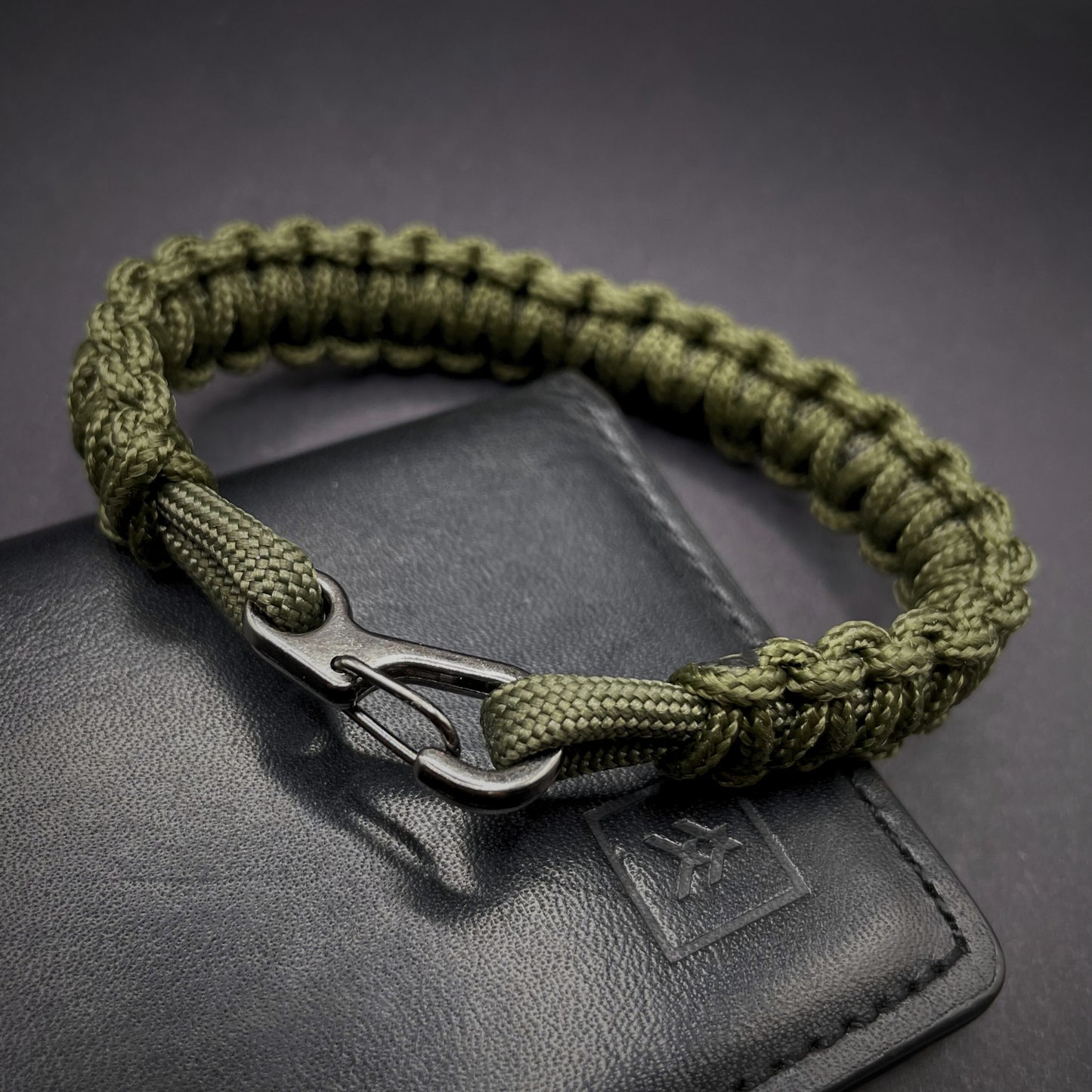 Flat lay of Army Green cobra knot paracord bracelet on a dark grey surface