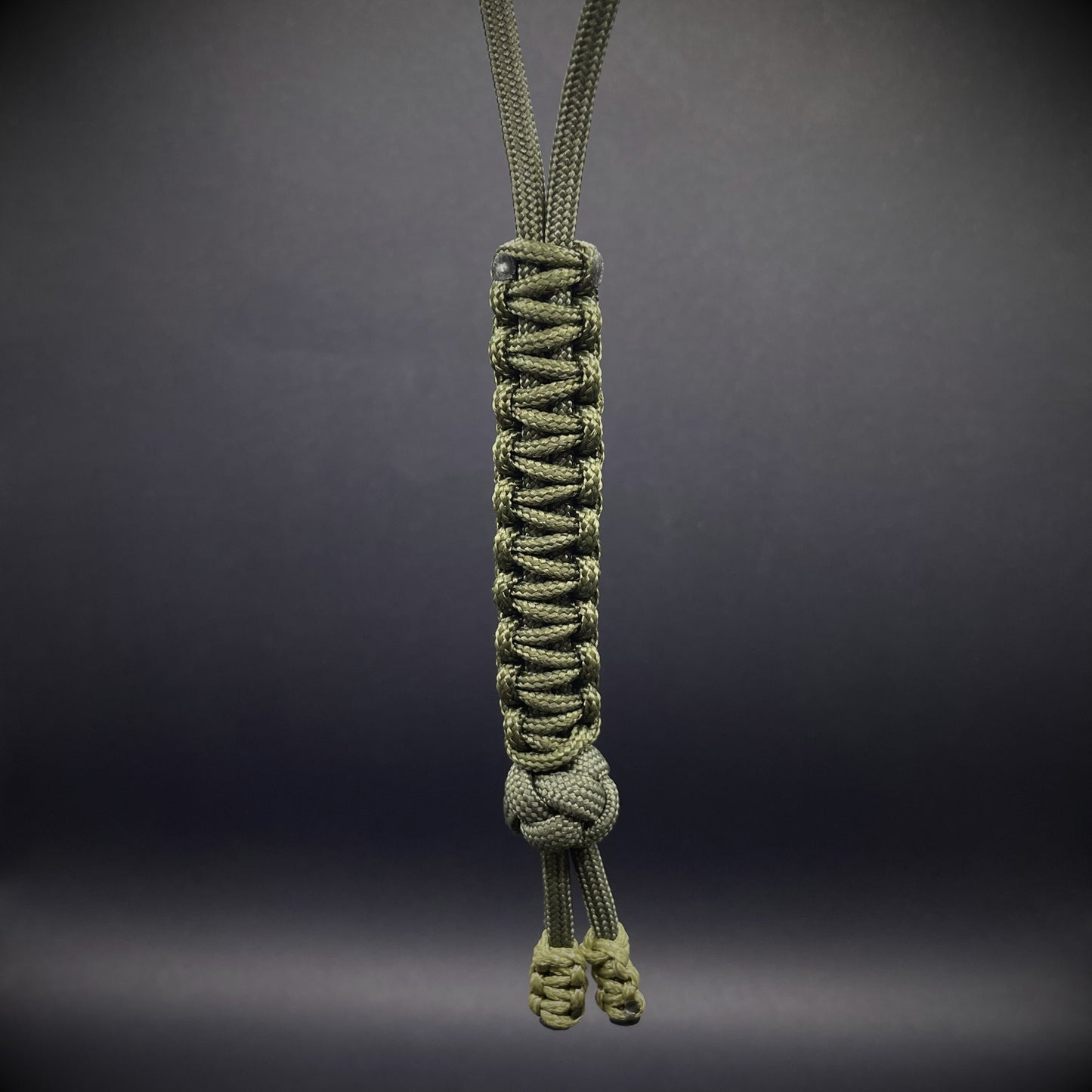 Flat lay of a army green 550 Paracord knife lanyards on a dark grey background