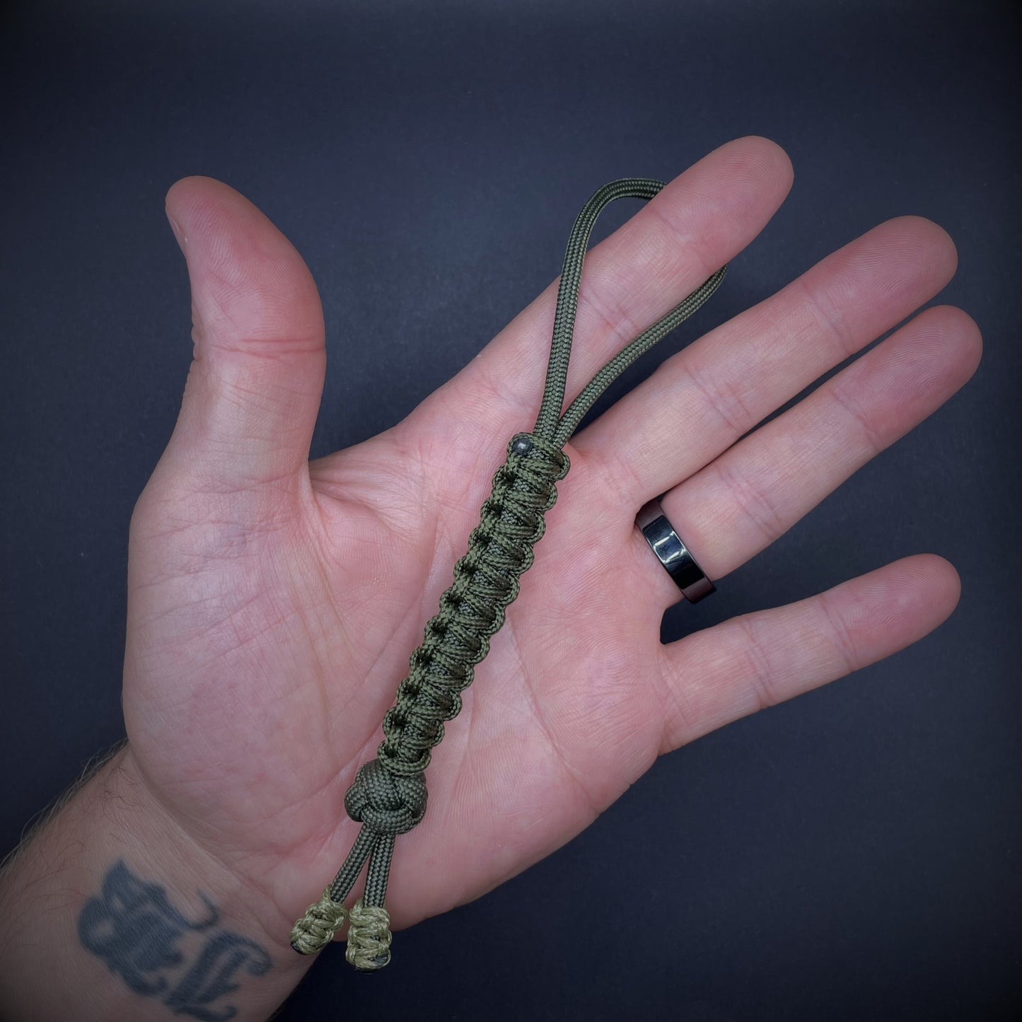 Flat lay of a army green 550 Paracord knife lanyards on a dark grey background