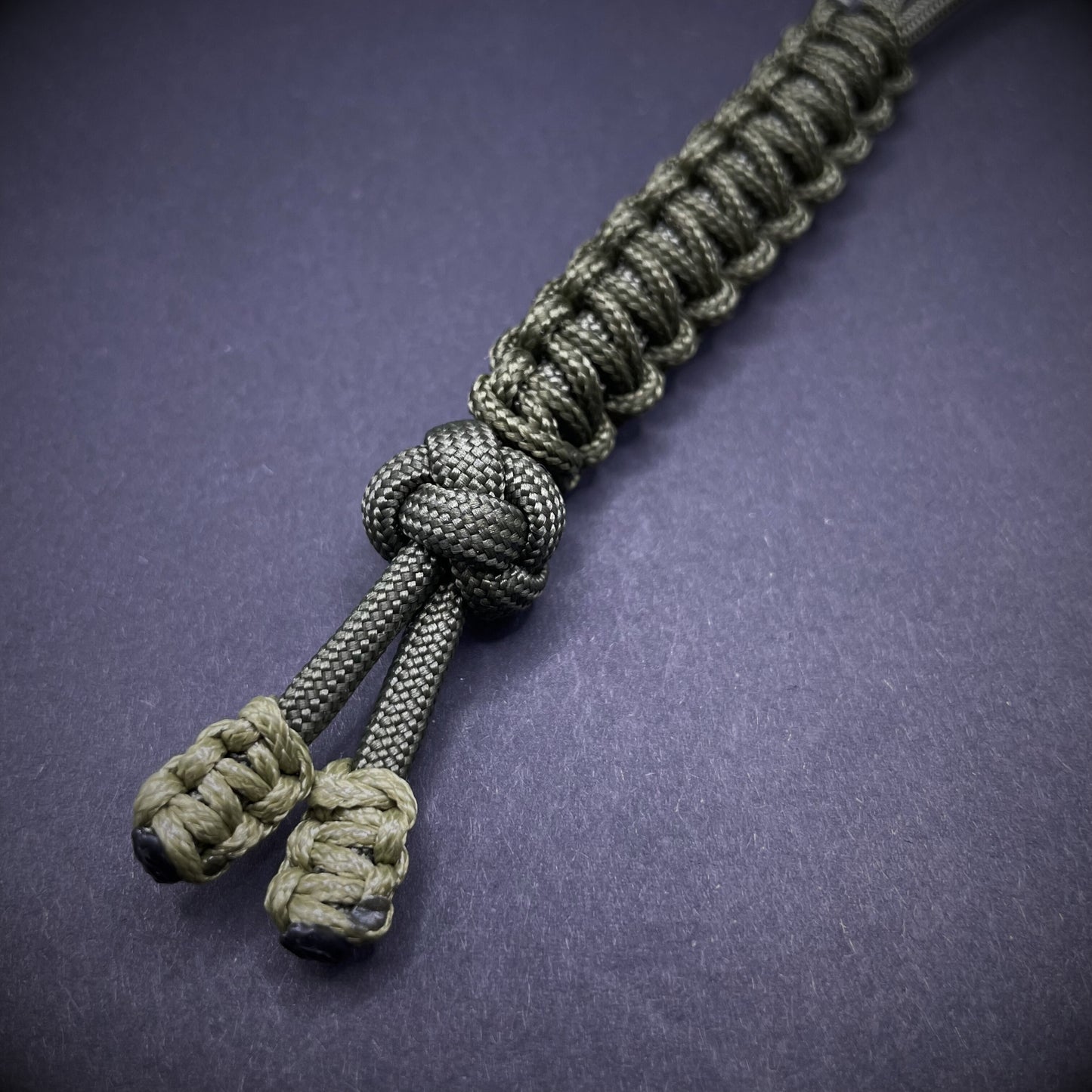 Flat lay of a army green 550 Paracord knife lanyards on a dark grey background