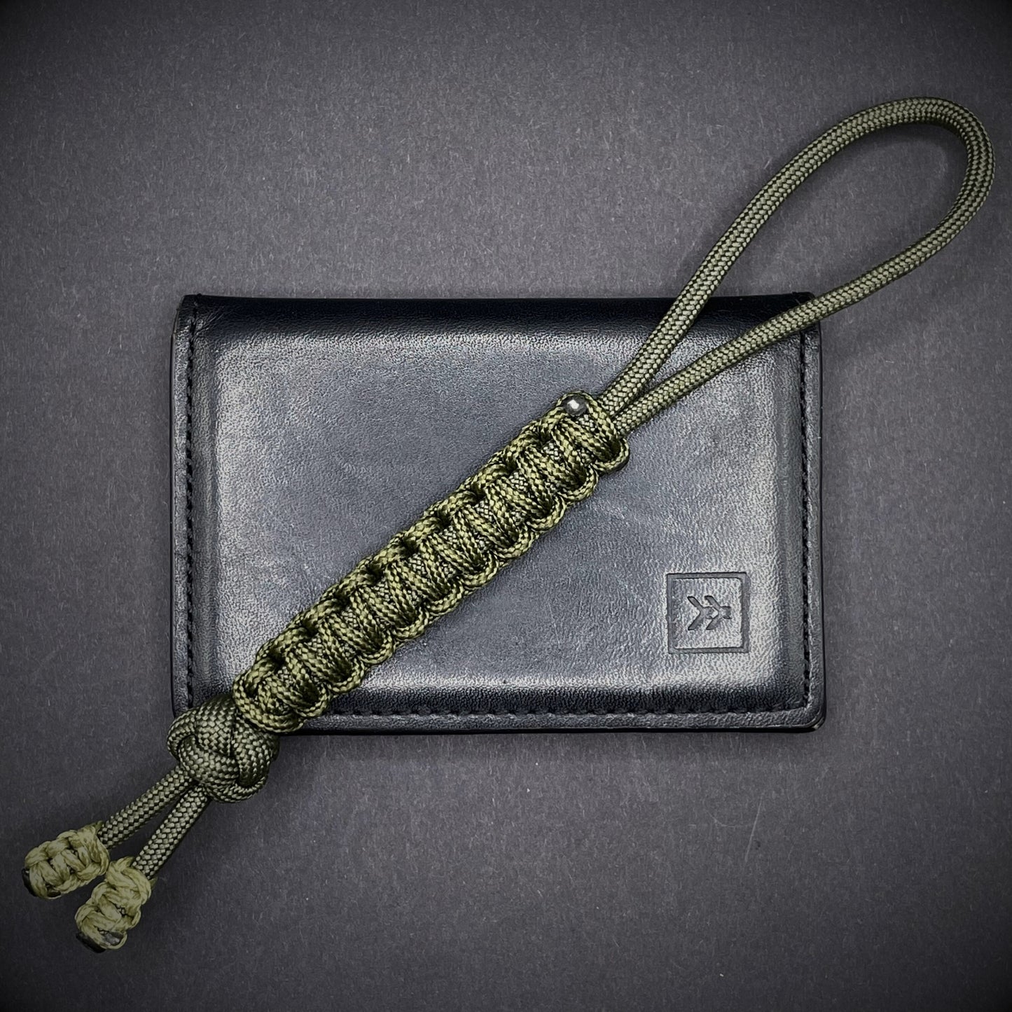 Flat lay of a army green 550 Paracord knife lanyards on a dark grey background