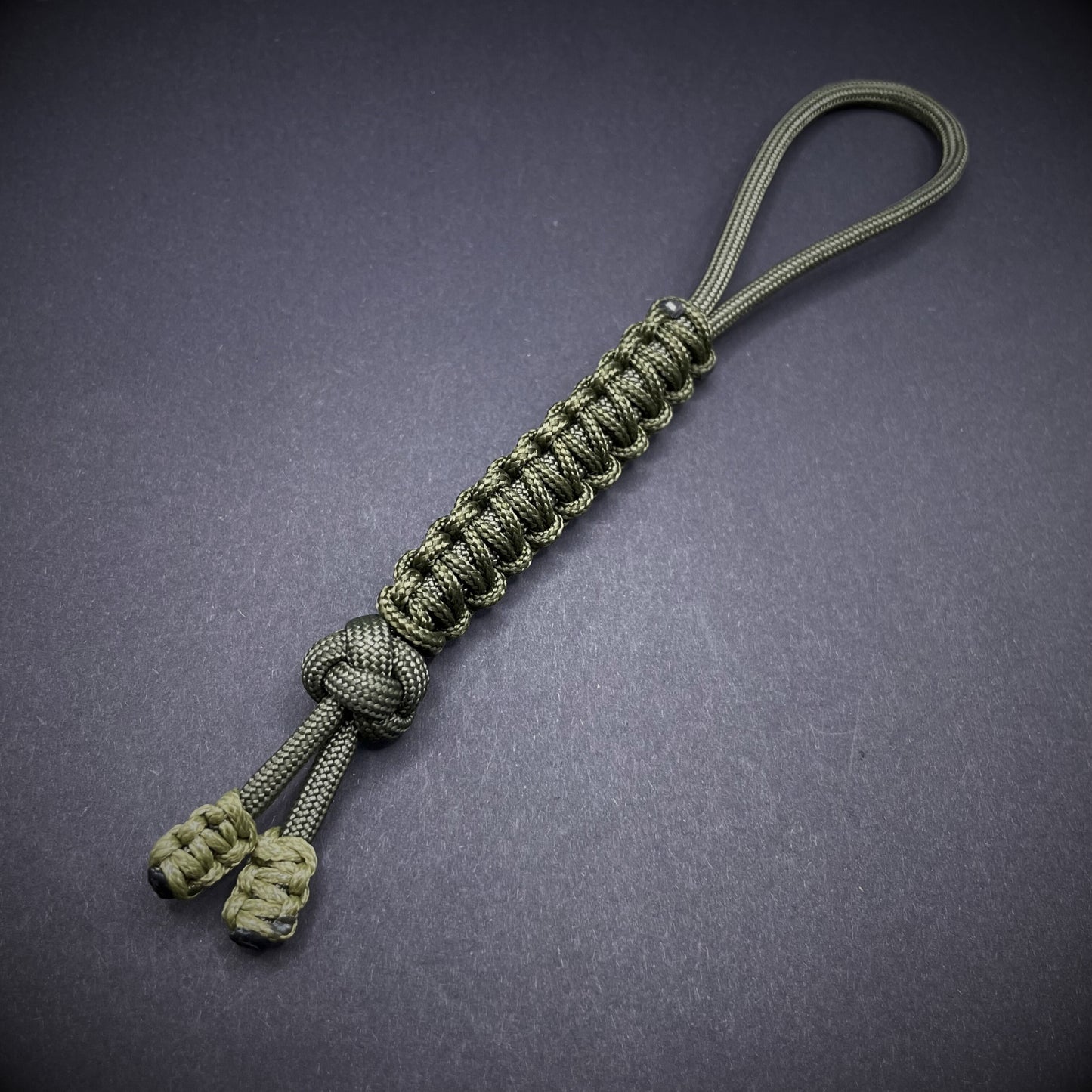 Flat lay of a army green 550 Paracord knife lanyards on a dark grey background
