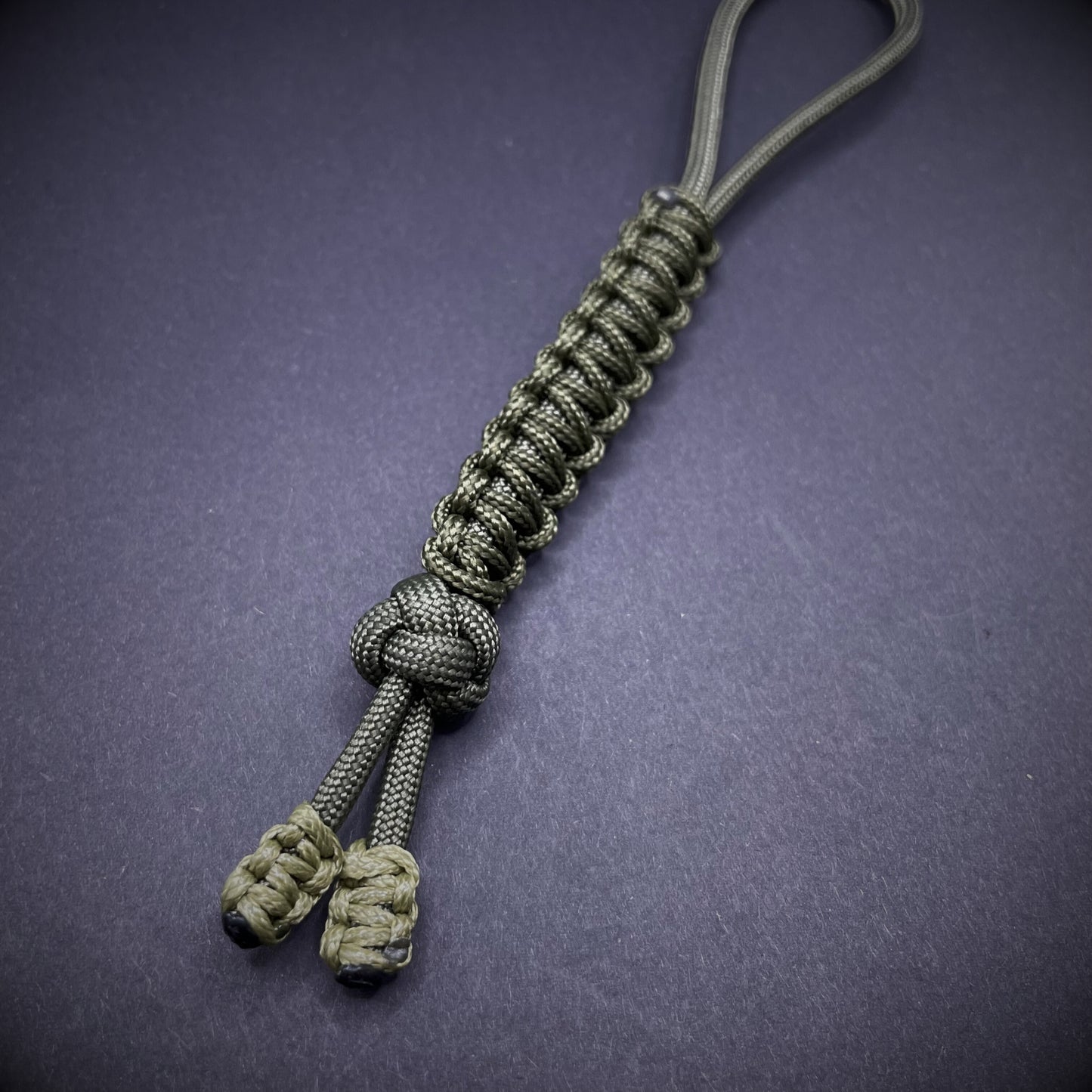 Flat lay of a army green 550 Paracord knife lanyards on a dark grey background