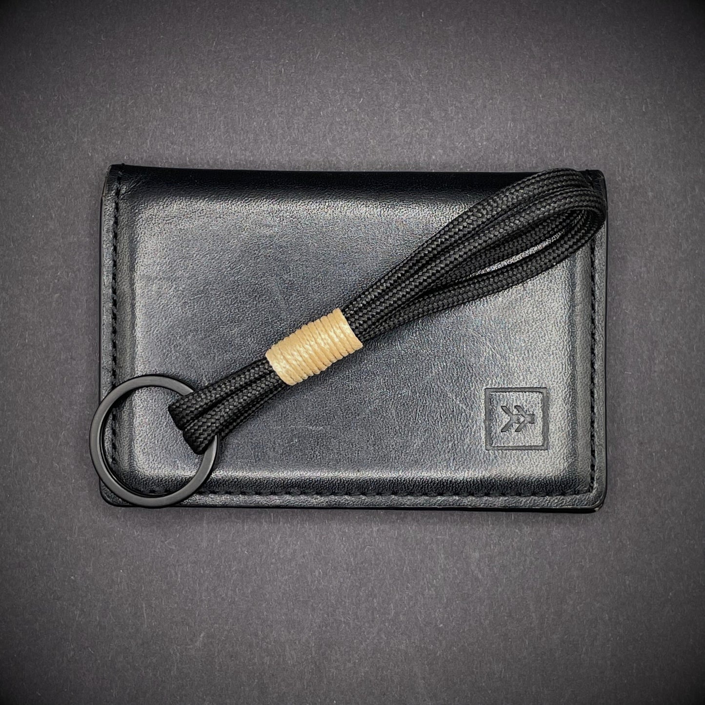 Flat lay of black 550 paracord keychain with tan cotton whipping on a dark background.