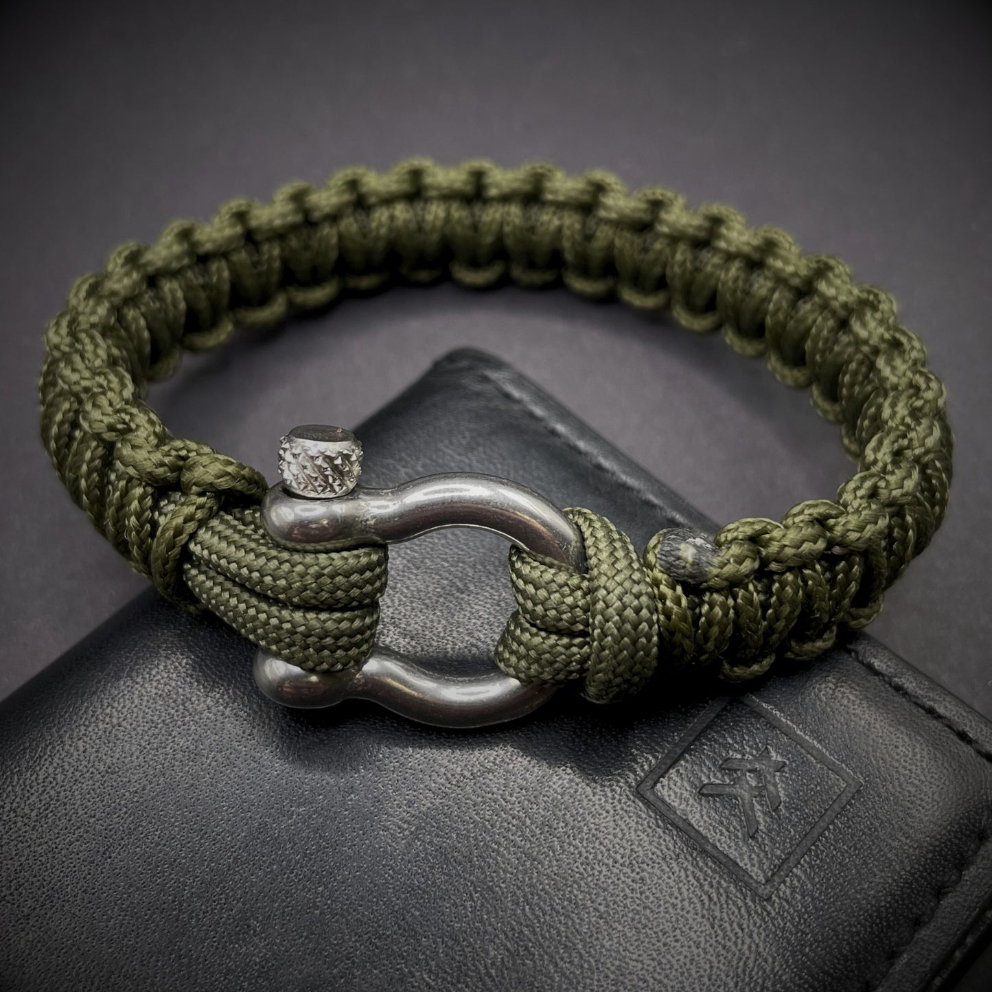 Flat lay of Army Green cobra knot paracord bracelet on a dark grey surface