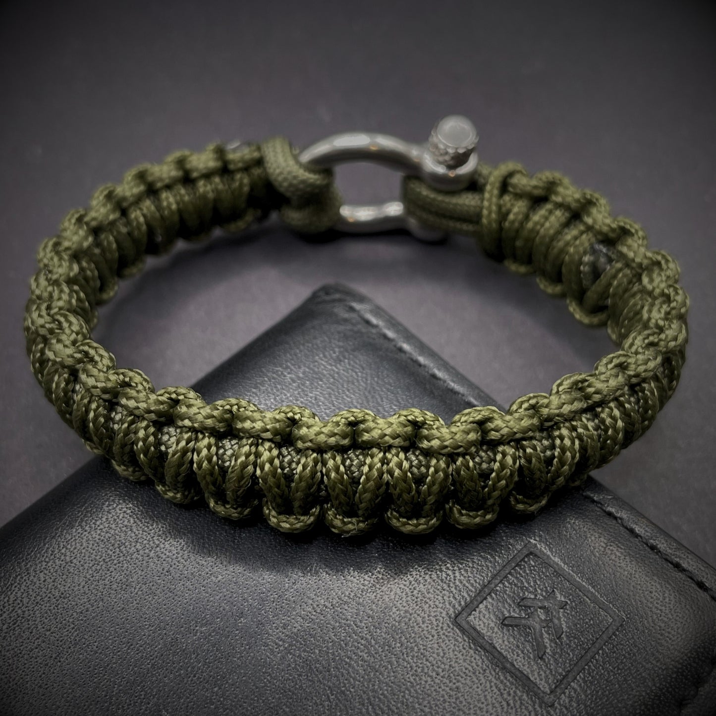 Flat lay of Army Green cobra knot paracord bracelet on a dark grey surface