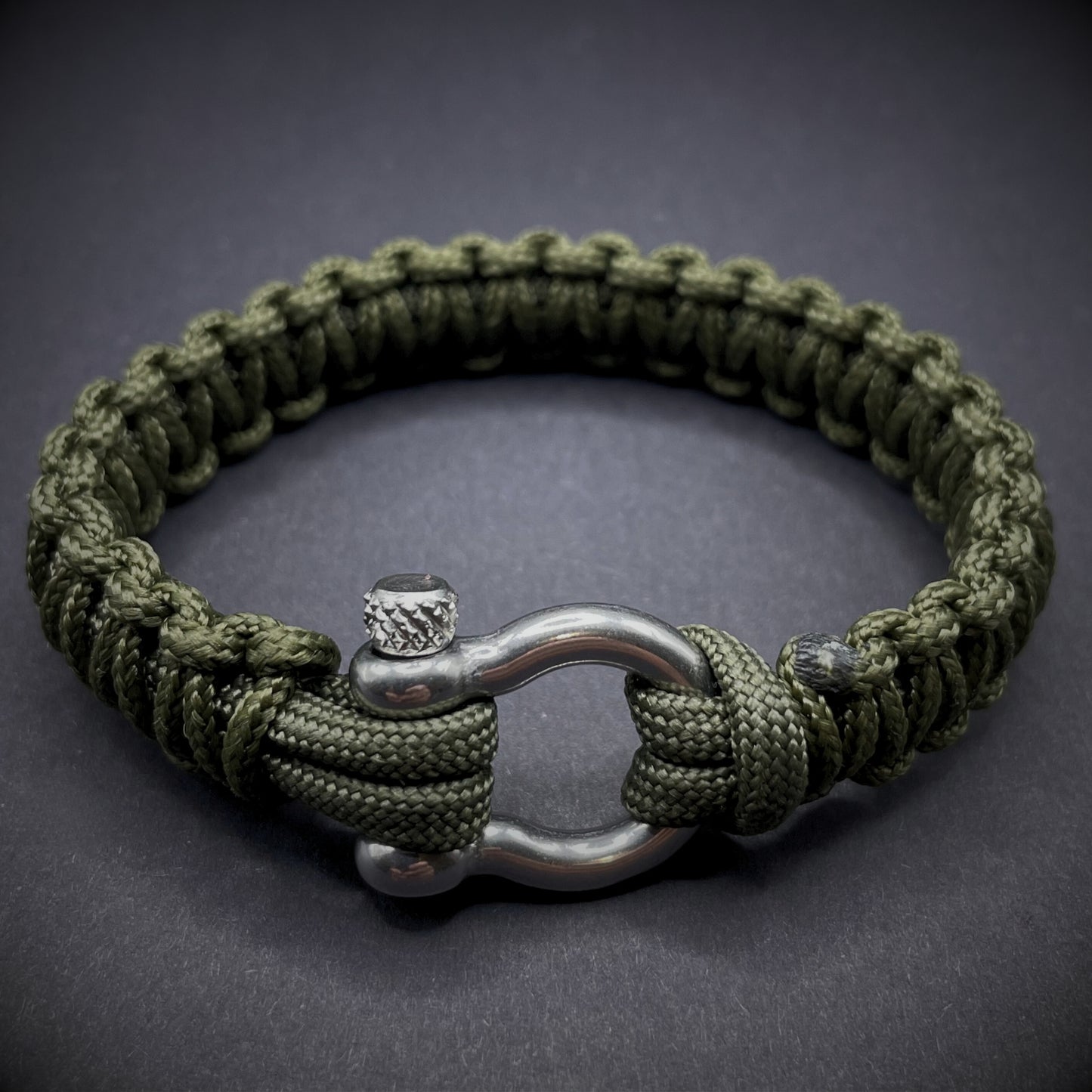Flat lay of Army Green cobra knot paracord bracelet on a dark grey surface