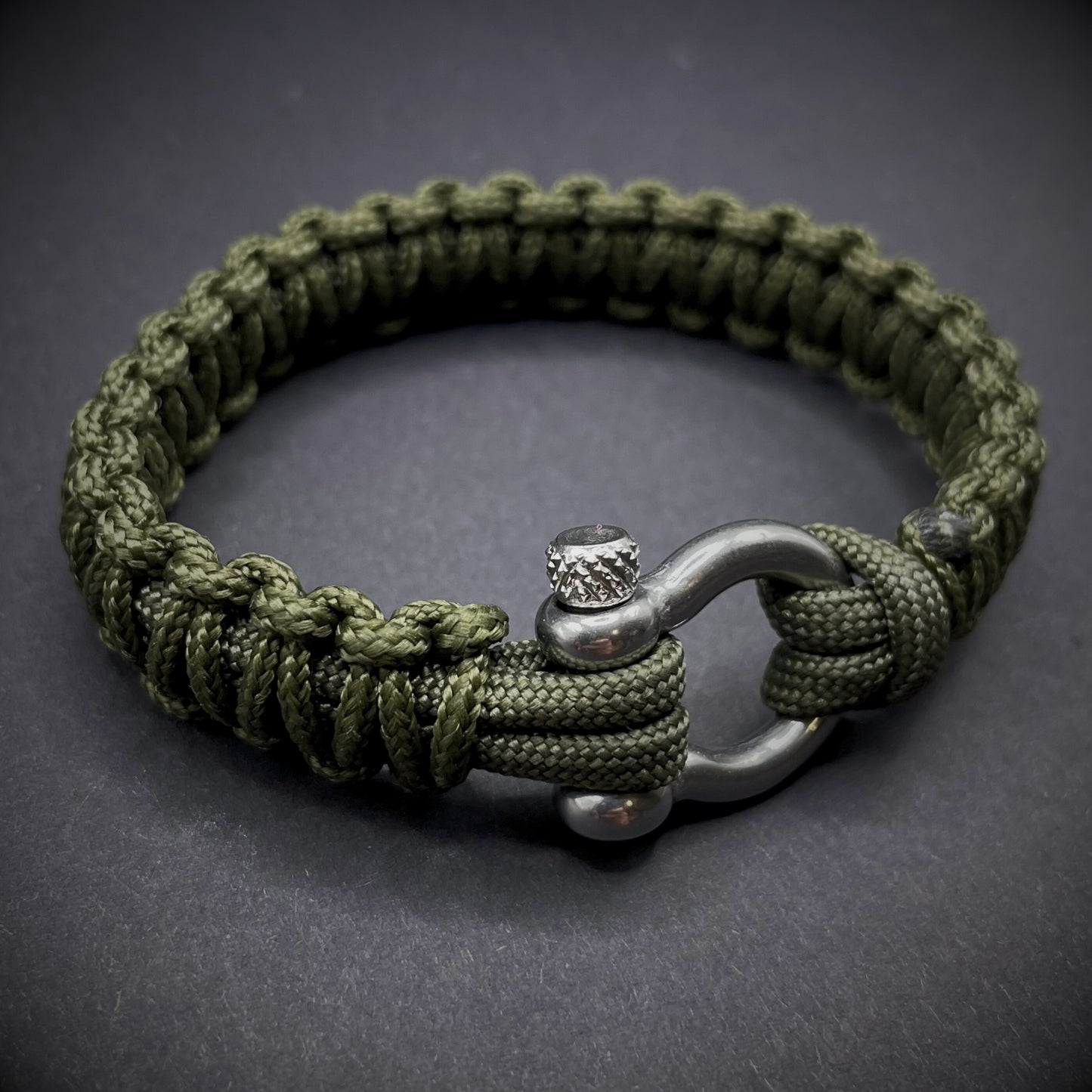 Flat lay of Army Green cobra knot paracord bracelet on a dark grey surface