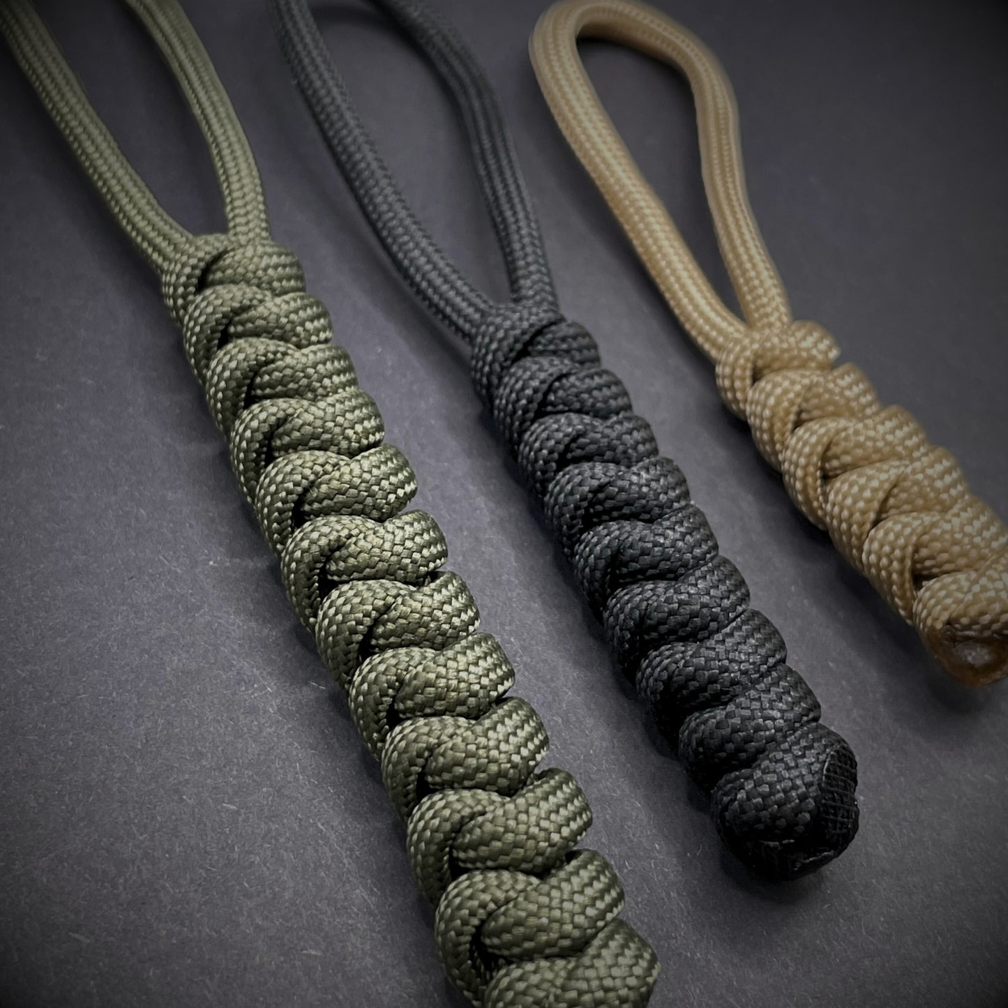 Flat lay of a 3 550 Paracord knife lanyards on a dark grey background