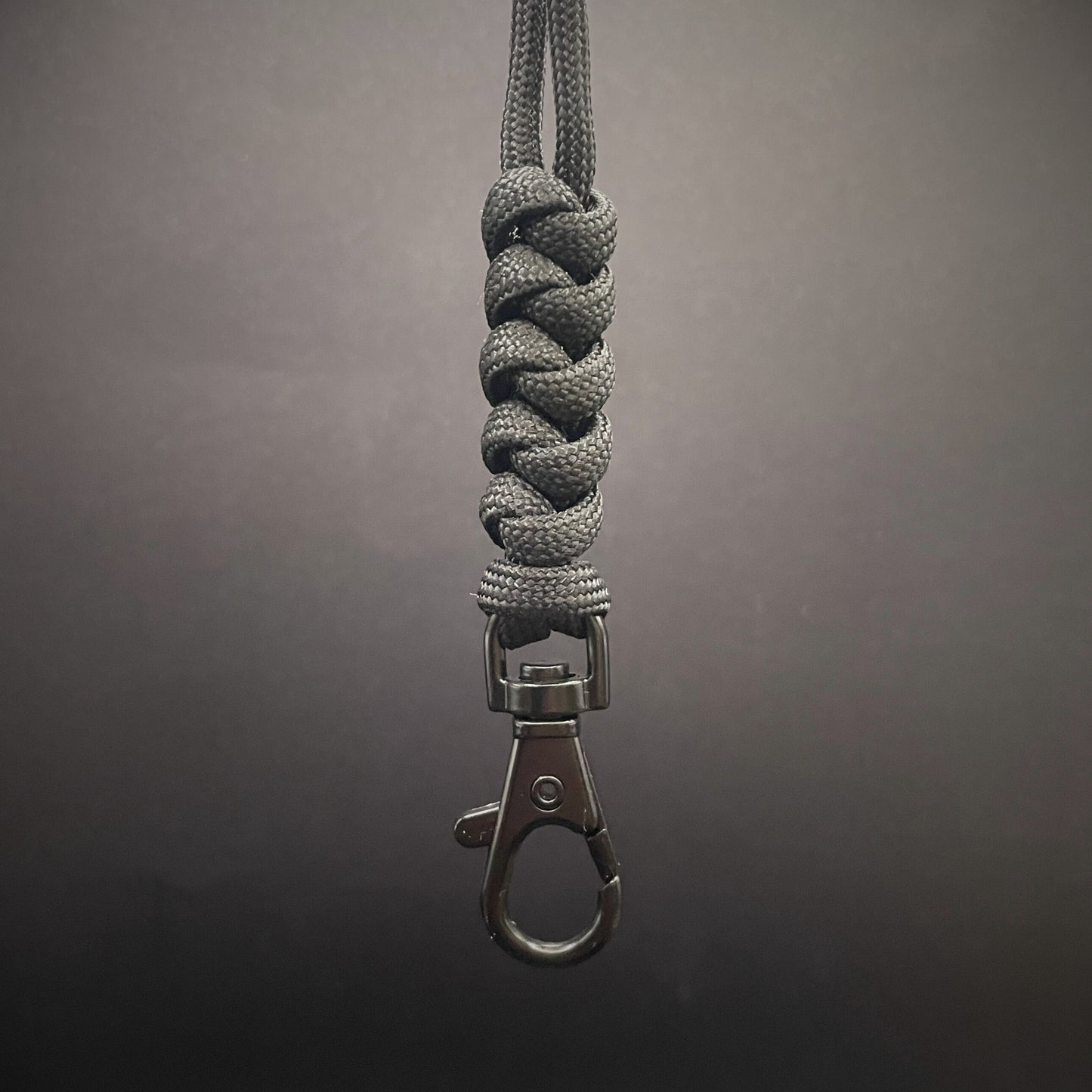 Black 550 Paracord snake knot lanyard with black lobster clasp, displayed on a dark textured background.