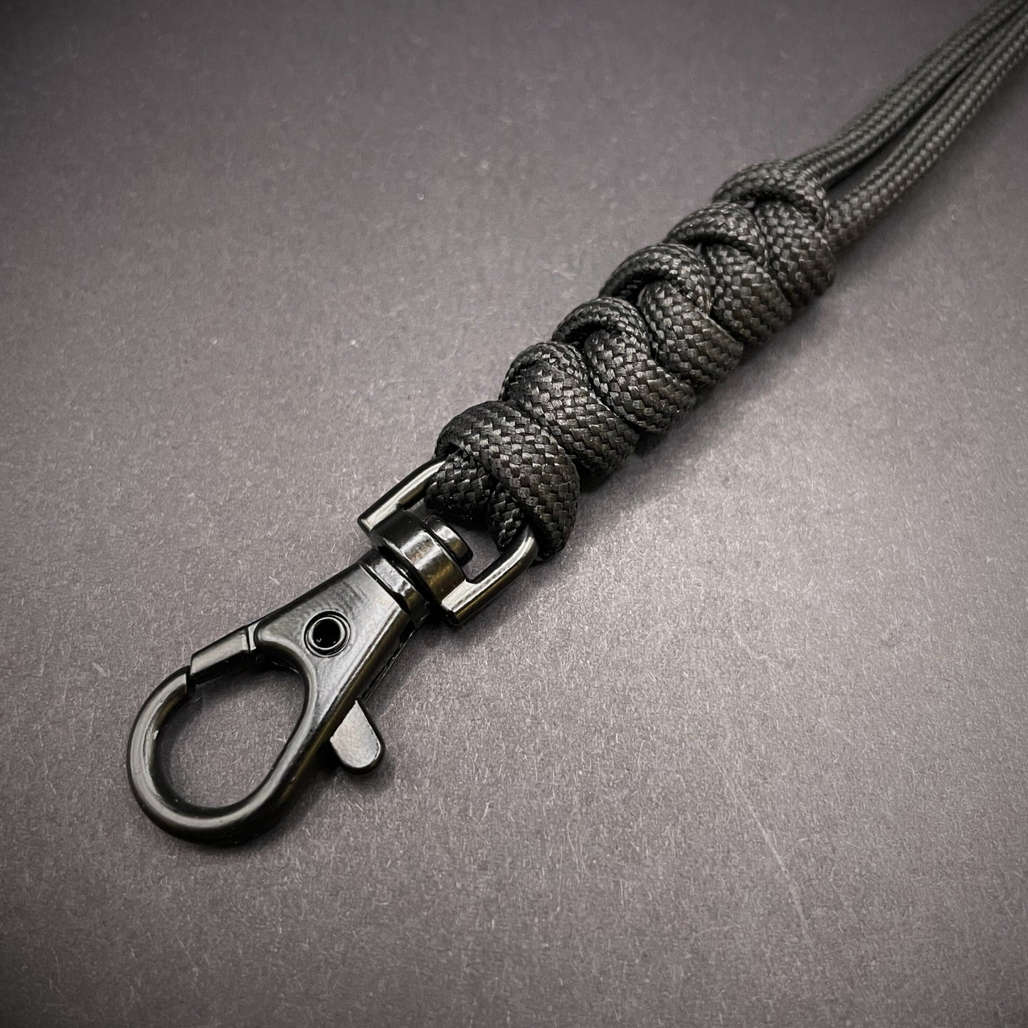 Black 550 Paracord snake knot lanyard with lobster clasp, displayed on a dark textured background.