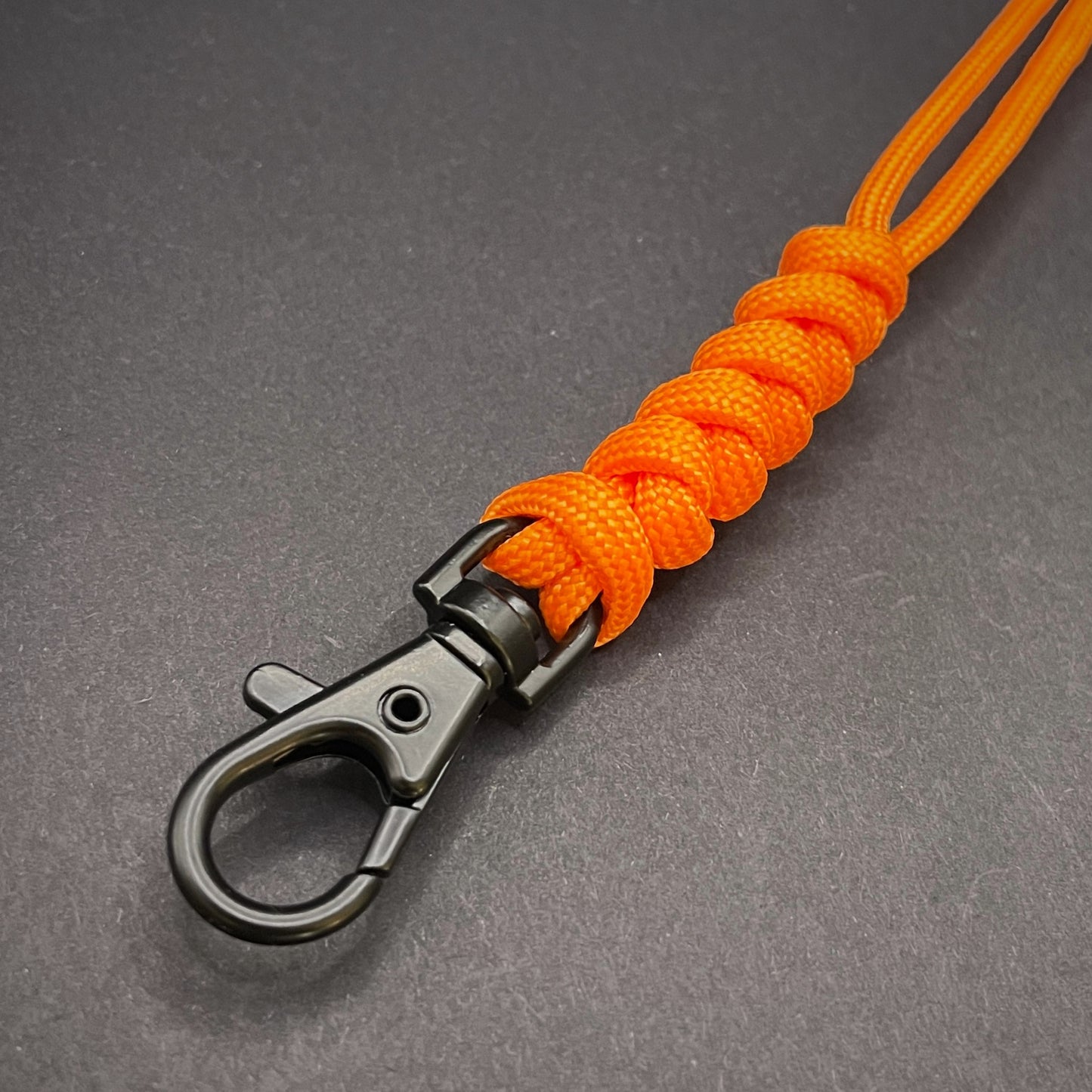 Orange 550 Paracord snake knot lanyard with lobster clasp, displayed on a dark textured background.
