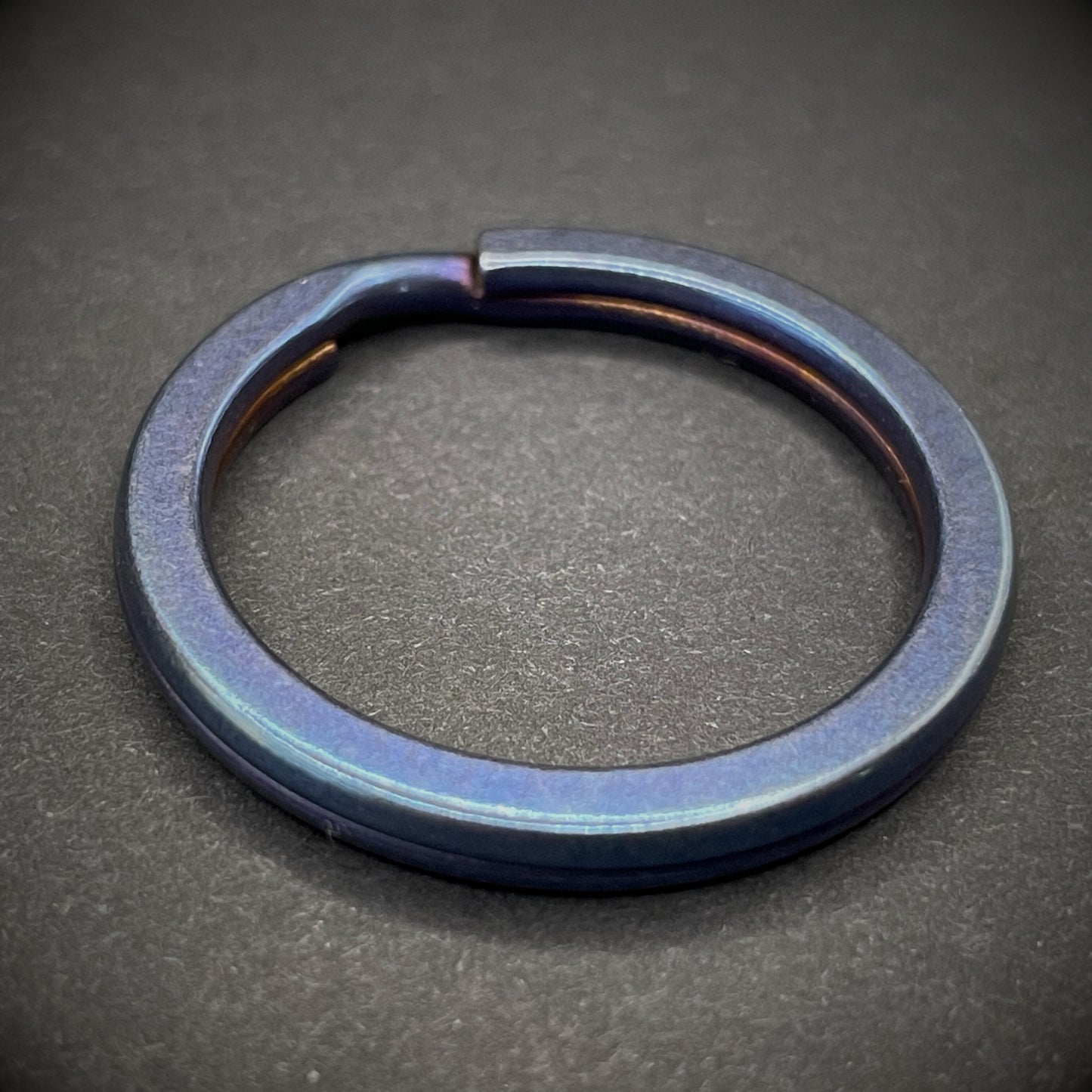 A Blue Titanium Split Ring on a dark grey background