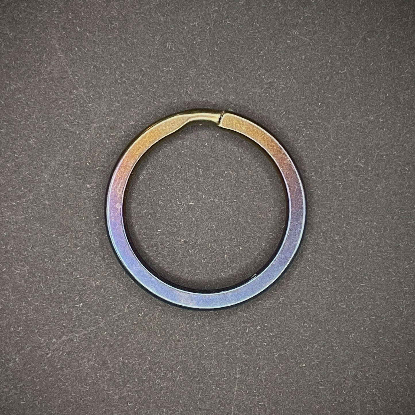 An Oil Slick Titanium Split Ring on a dark grey background