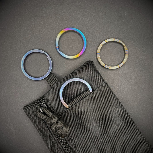A group of Titanium Split Rings on a dark grey background, one is attached to a black pouch