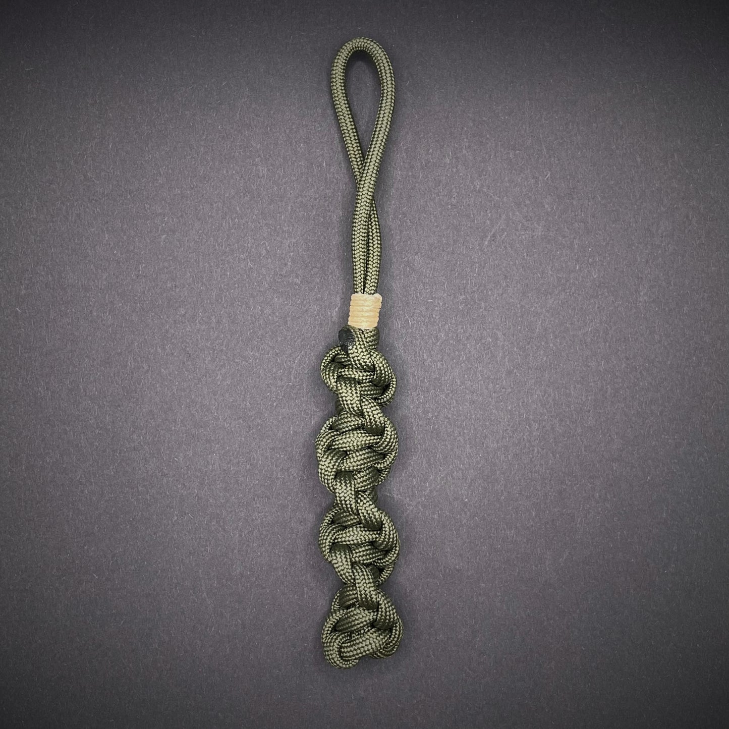 Flat lay of an Army Green 550 Paracord knife lanyards on a dark grey background