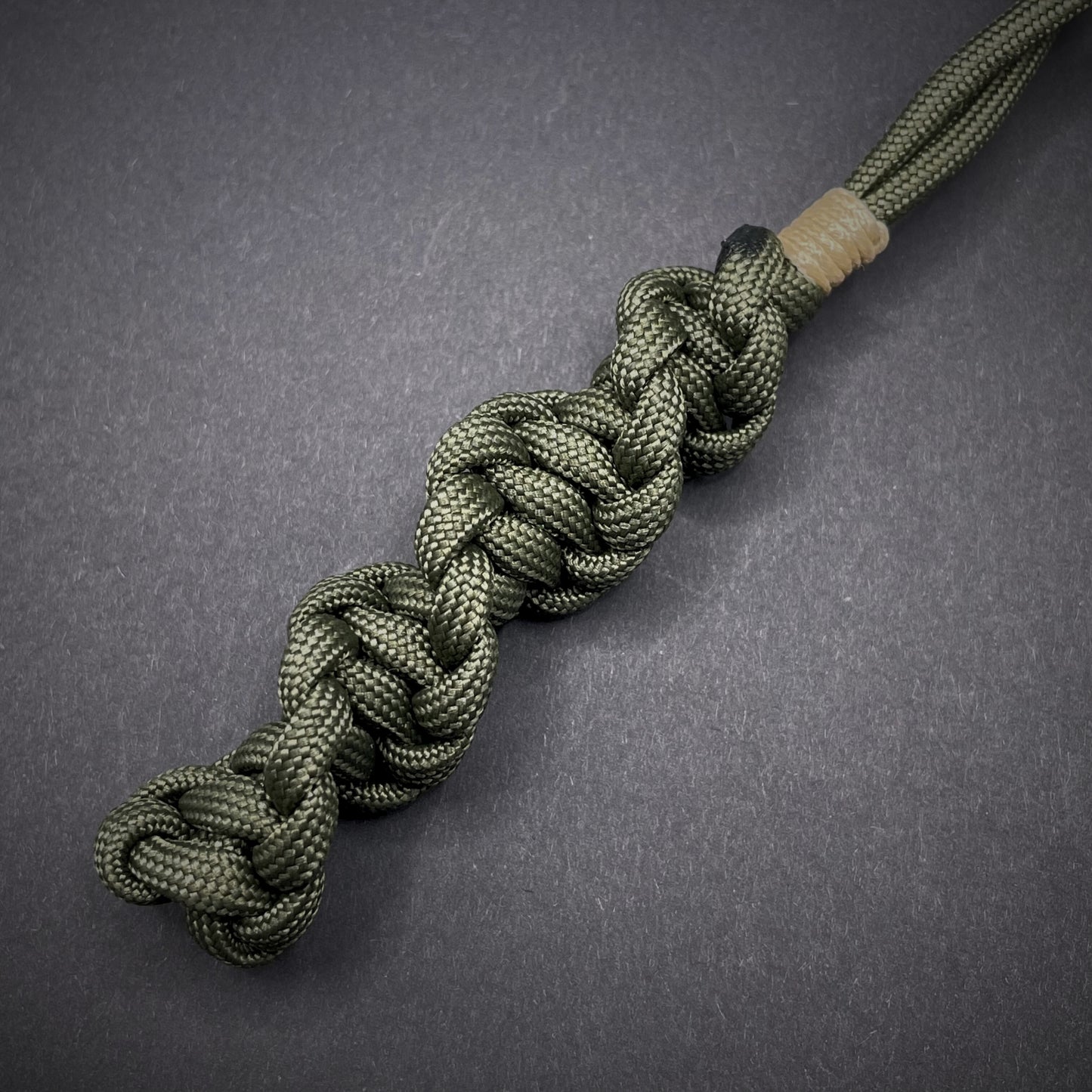 Flat lay of an Army Green 550 Paracord knife lanyards on a dark grey background