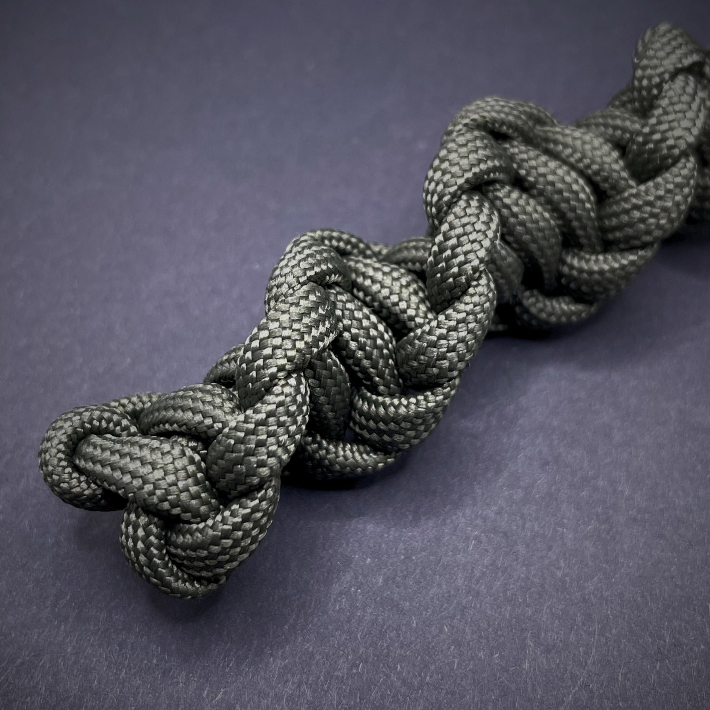 Flat lay of an Army Green 550 Paracord knife lanyards on a dark grey background