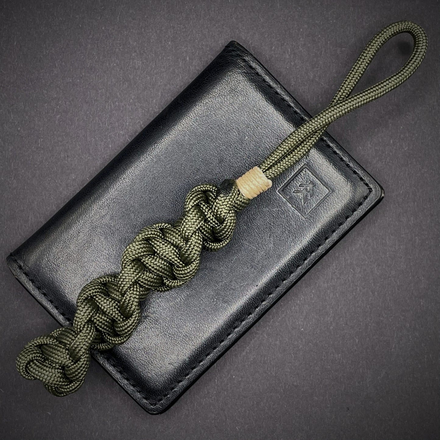 Flat lay of an Army Green 550 Paracord knife lanyards on a dark grey background