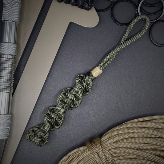 Flat lay of an Army Green 550 Paracord knife lanyards on a dark grey background surrounded by EDC items