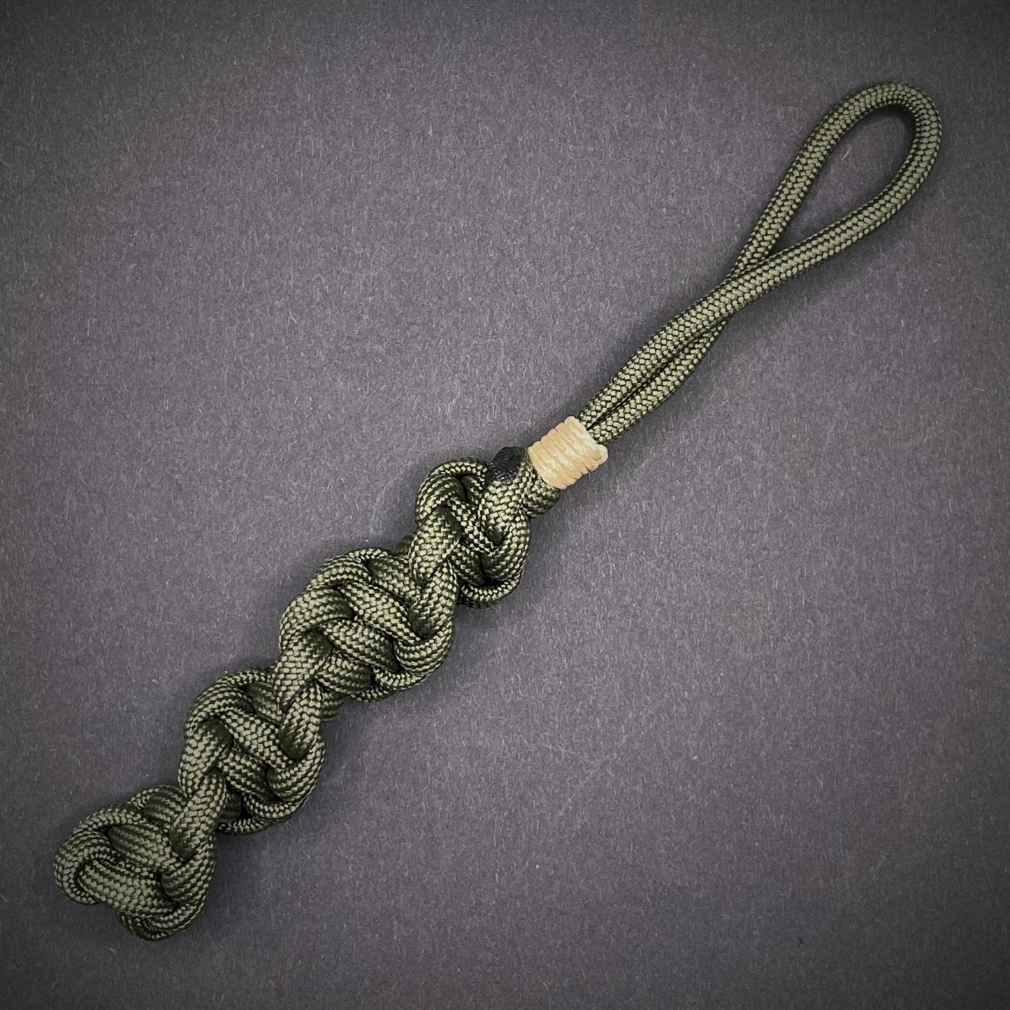 Flat lay of an Army Green 550 Paracord knife lanyards on a dark grey background