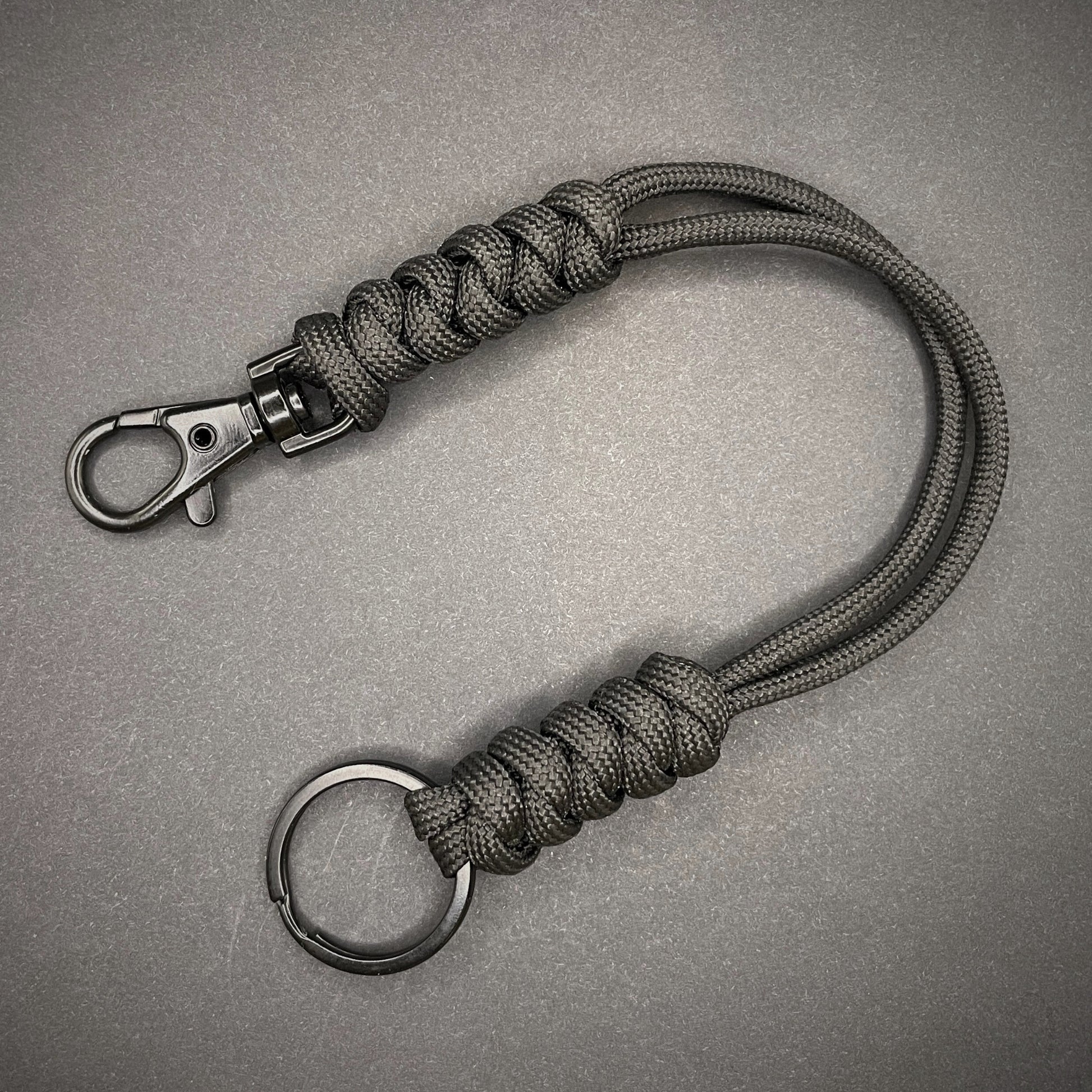Black 550 Paracord snake knot lanyard with black split ring and lobster clasp, displayed on a dark textured background.
