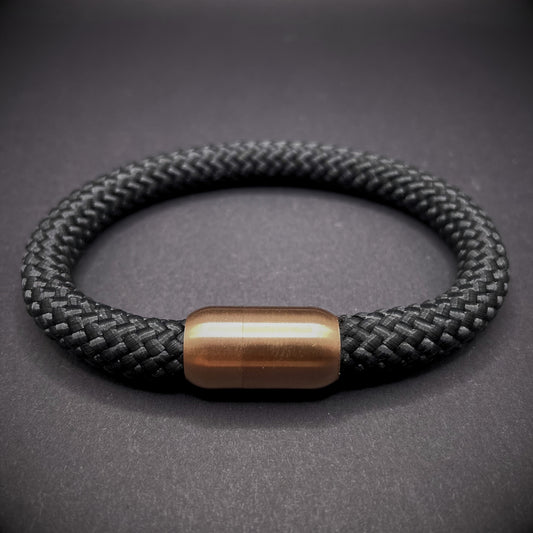 Black braided rope bracelet with a sleek cylindrical rose gold metal clasp, displayed on a dark textured background.