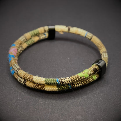 Khaki Boho rope bracelet with black sliding clasps, displayed on a dark grey surface.