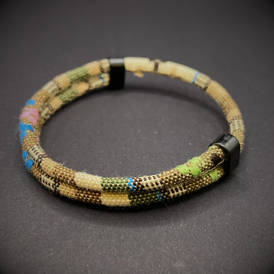 Khaki Boho rope bracelet with black sliding clasps, displayed on a dark grey surface.