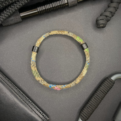 Khaki Boho rope bracelet with black sliding clasps, displayed on a dark grey surface with EDC gear in the background.