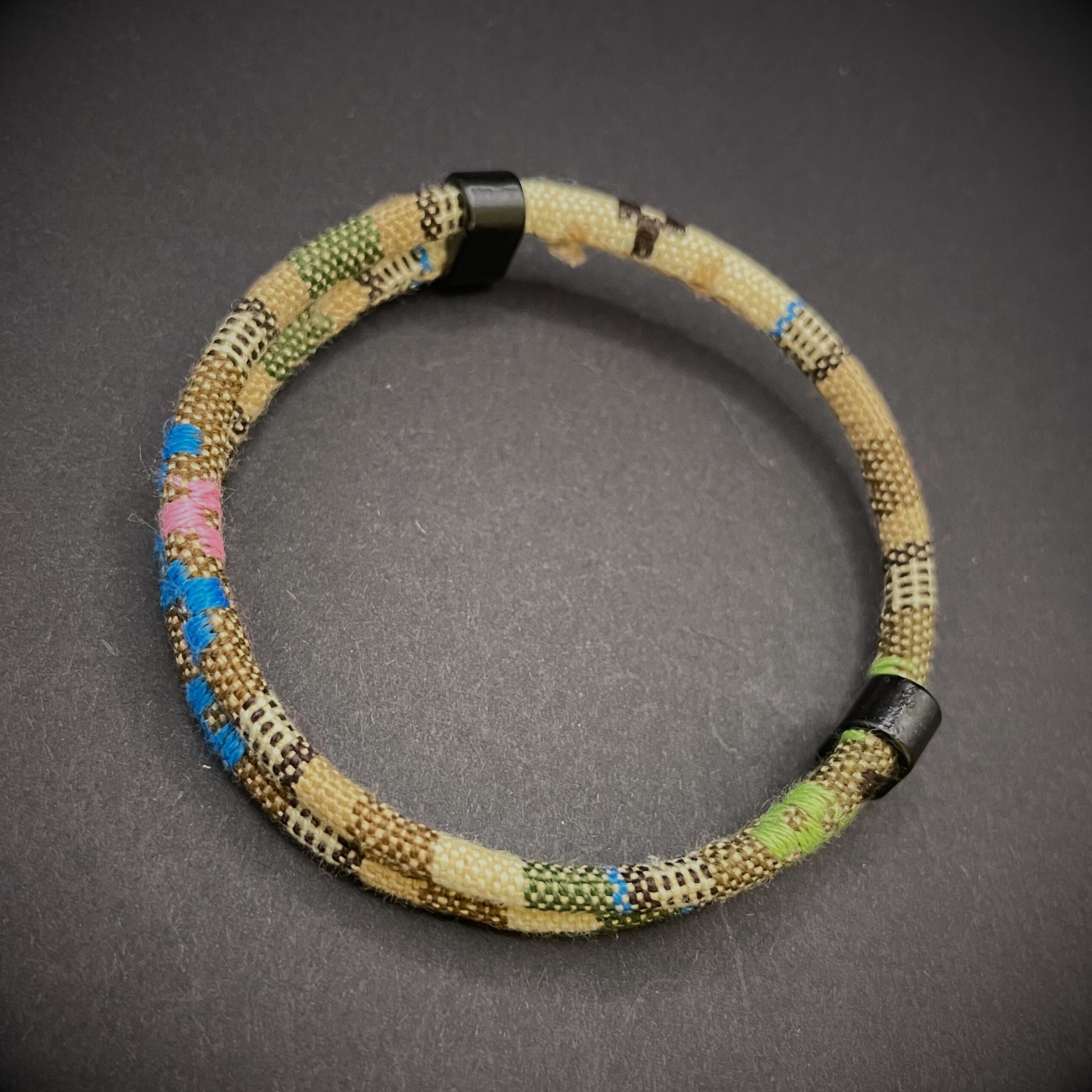 Khaki Boho rope bracelet with black sliding clasps, displayed on a dark grey surface.
