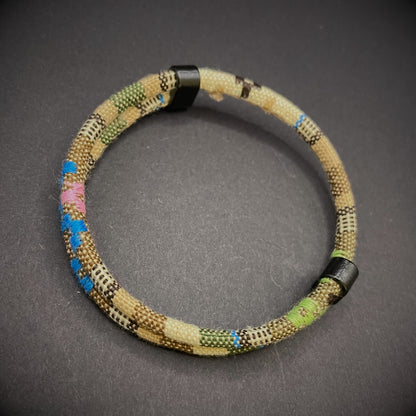 Khaki Boho rope bracelet with black sliding clasps, displayed on a dark grey surface.