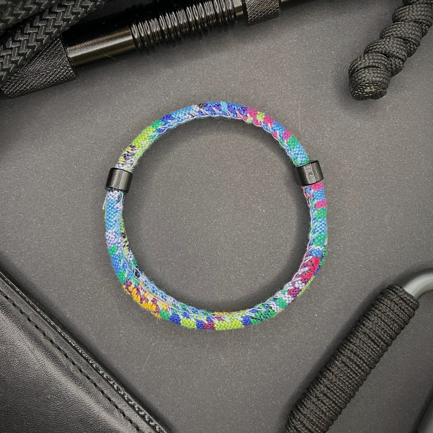 Light Blue Boho rope bracelet with black sliding clasps, displayed on a dark grey surface with EDC gear in the background.