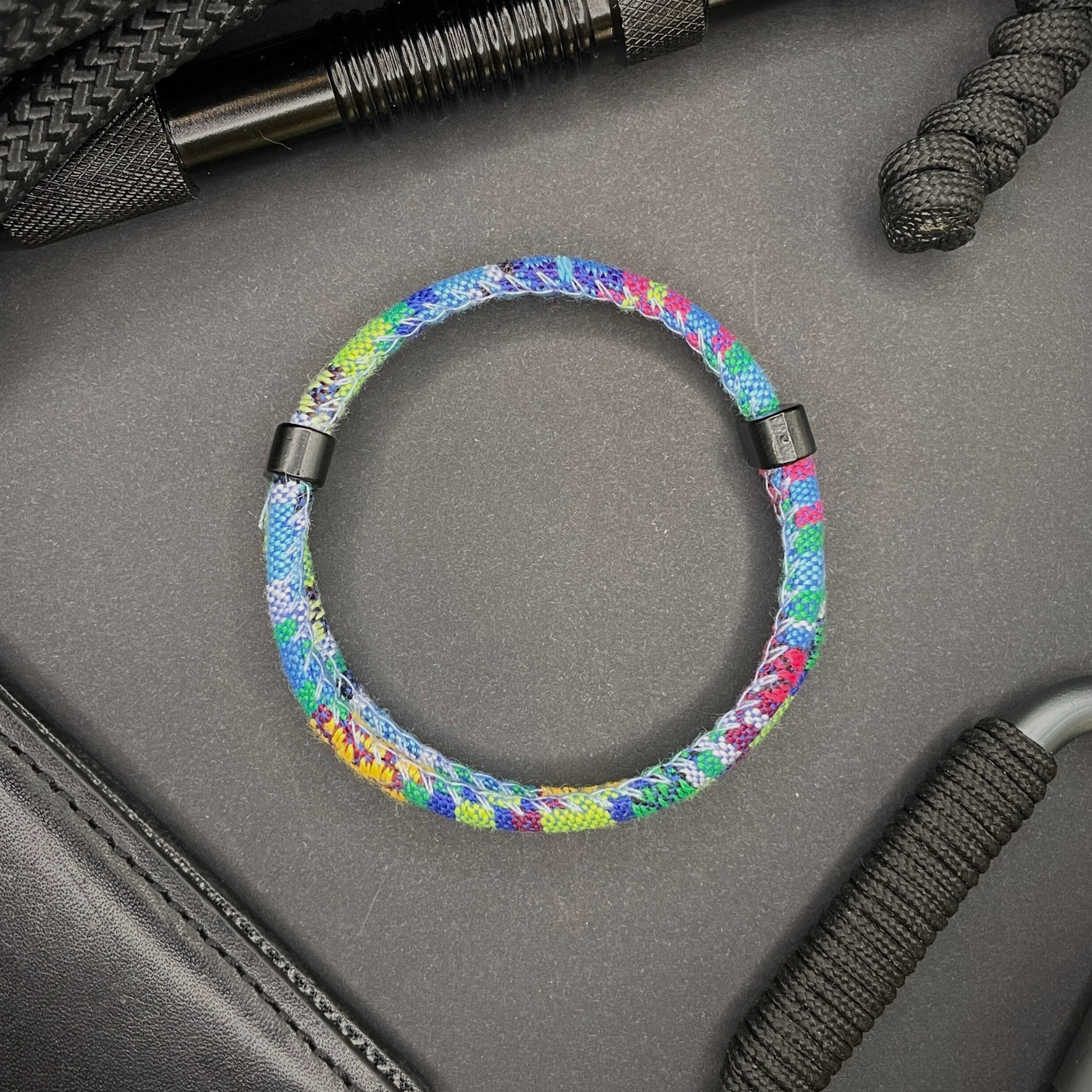 Light Blue Boho rope bracelet with black sliding clasps, displayed on a dark grey surface with EDC gear in the background.
