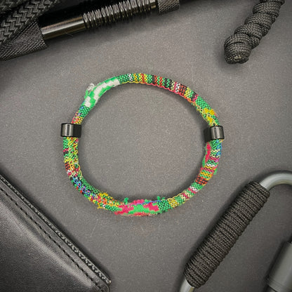 Green Boho rope bracelet with black sliding clasps, displayed on a dark grey surface with EDC gear in the background.