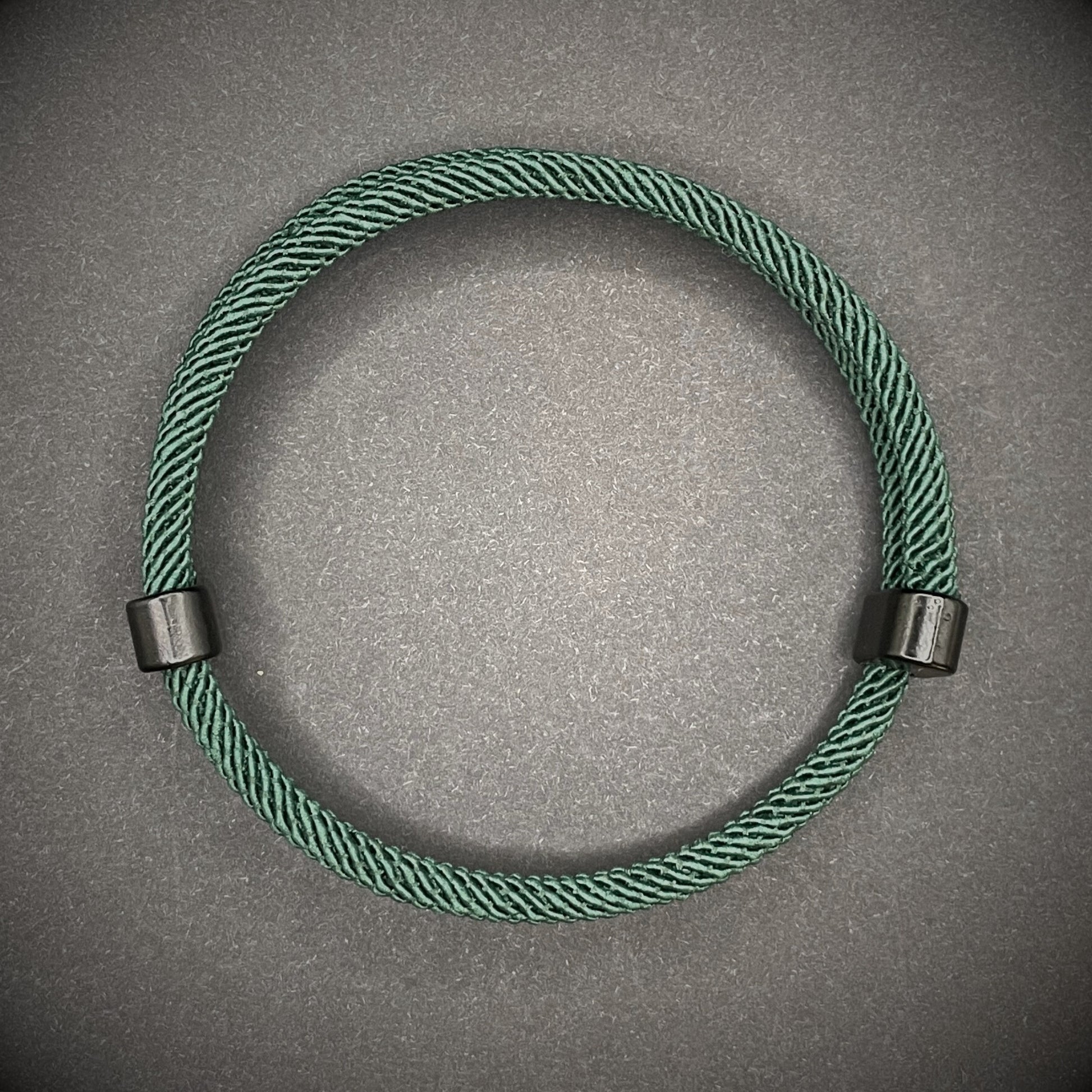 Forrest Green Milan rope bracelet with black sliding clasps, displayed on a dark grey surface.