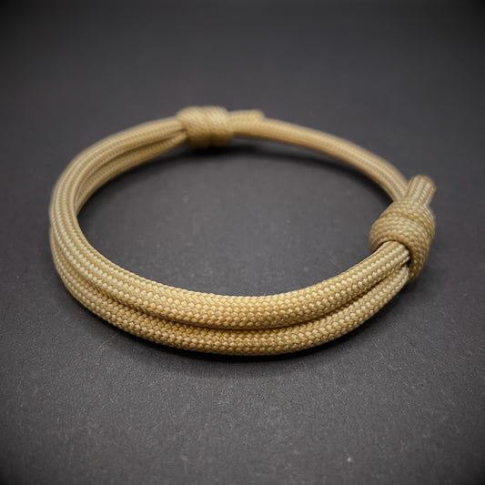 An khaki paracord rope bracelet arranged on a dark grey surface.