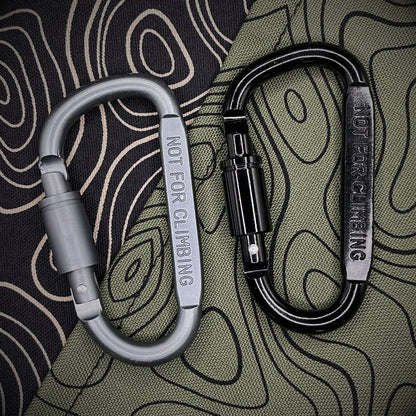 Black and grey carabiners marked 'NOT FOR CLIMBING' against a black background with topographic line pattern.