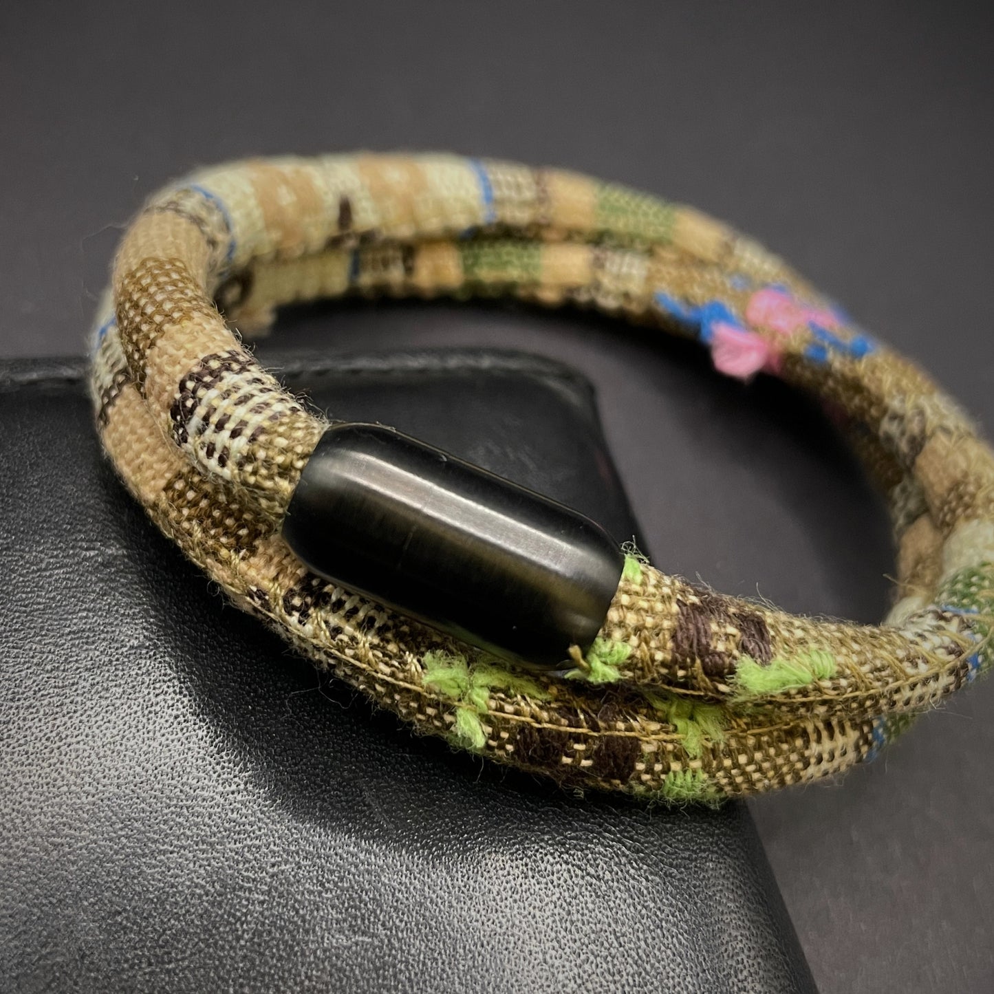 Khaki Boho rope bracelet with black magnetic clasps, displayed on a dark grey surface.