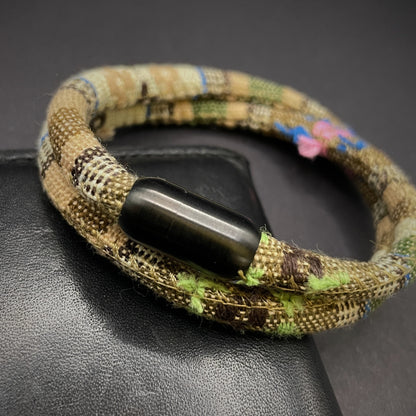 Khaki Boho rope bracelet with black magnetic clasps, displayed on a dark grey surface.
