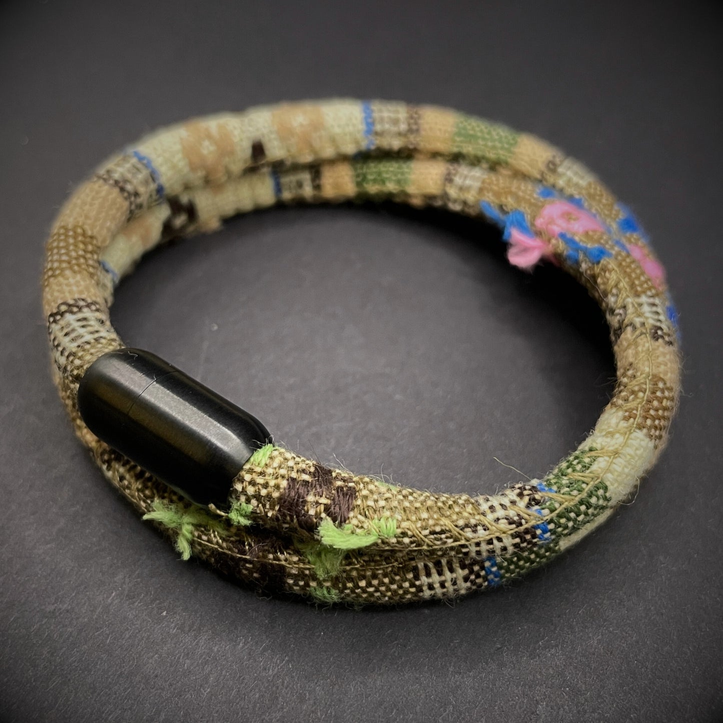 Khaki Boho rope bracelet with black magnetic clasps, displayed on a dark grey surface.