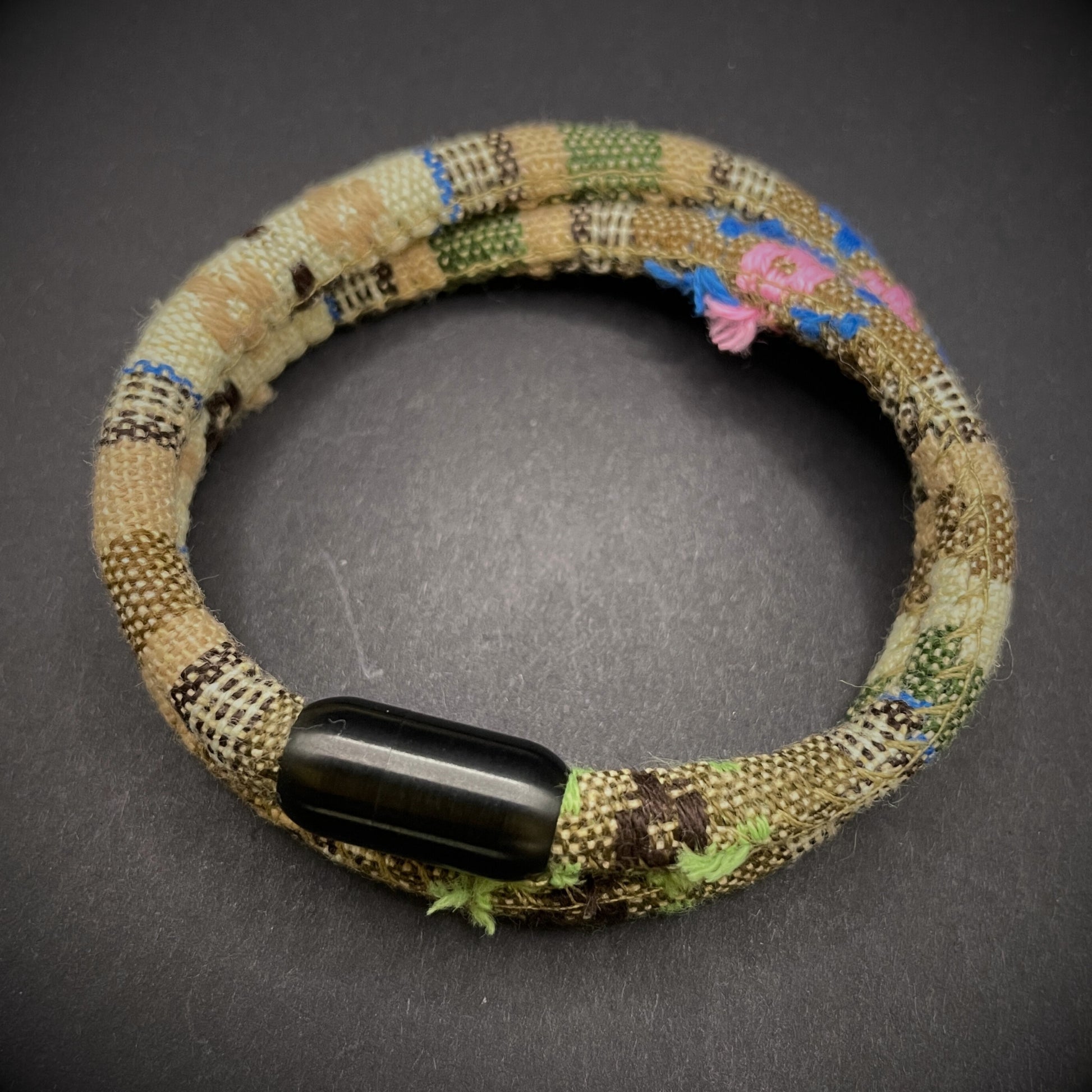 Khaki Boho rope bracelet with black magnetic clasps, displayed on a dark grey surface.