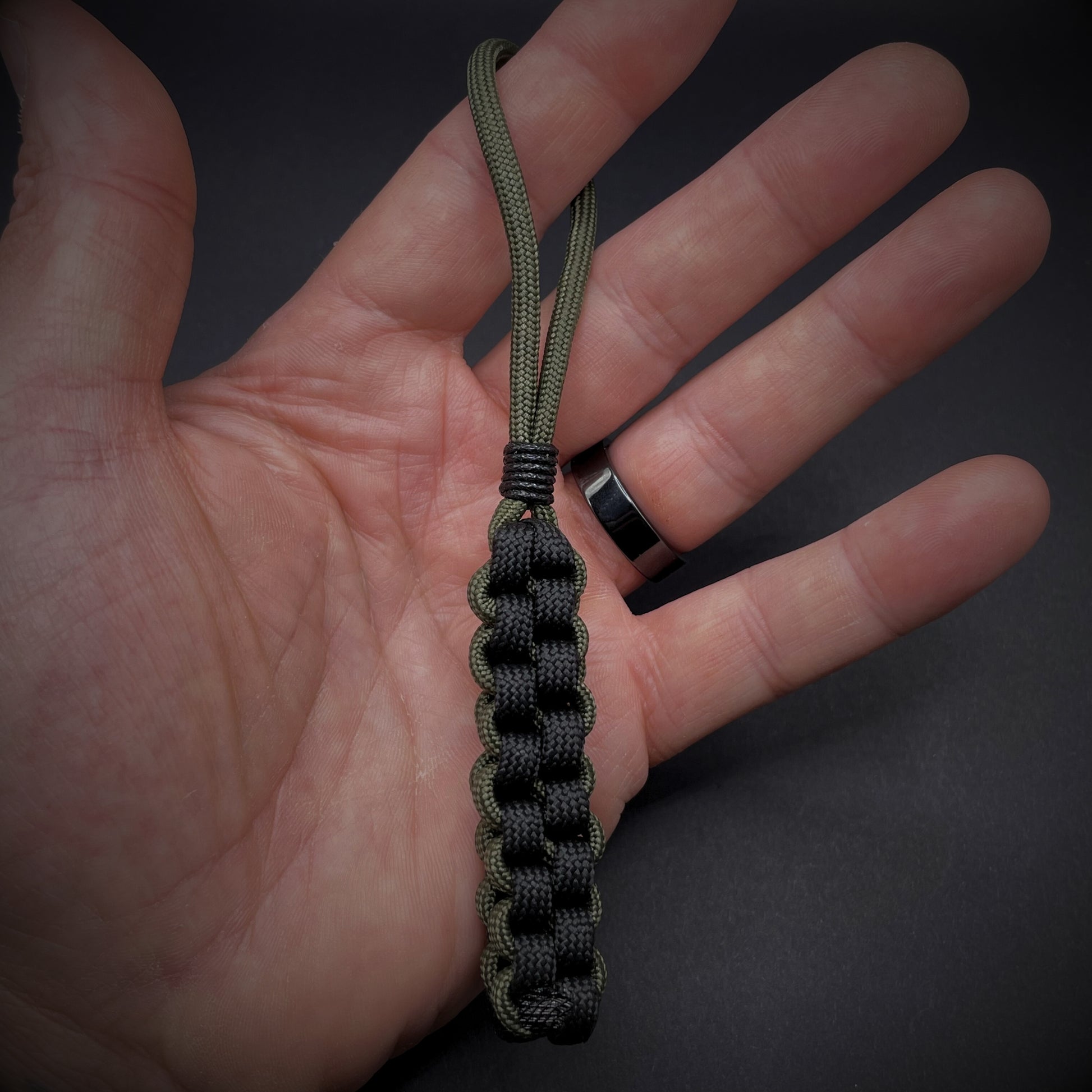 Flat lay of a 550 Paracord knife lanyard on a dark grey background in an open palmed hand