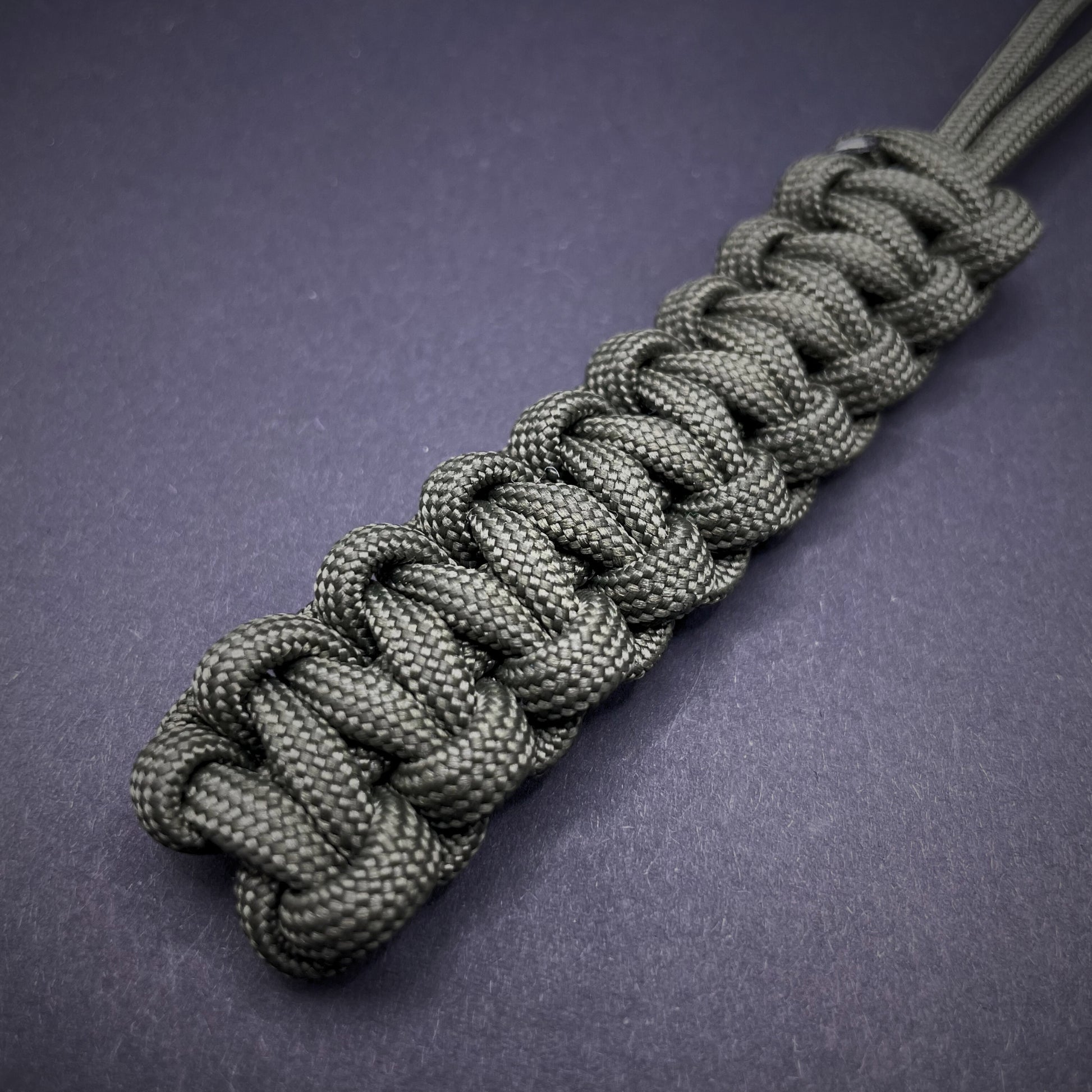 Flat lay of Army Green 550 Paracord knife lanyard on a dark grey background