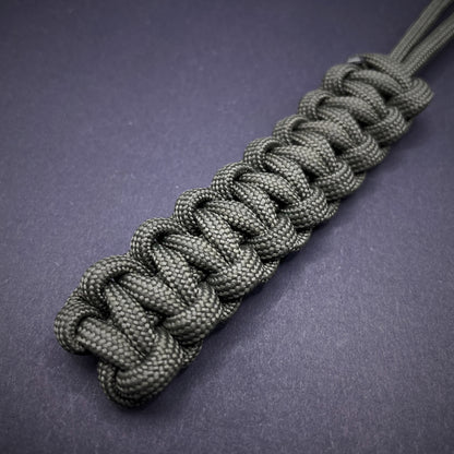 Flat lay of Army Green 550 Paracord knife lanyard on a dark grey background