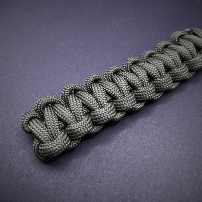 Flat lay of Army Green 550 Paracord knife lanyard on a dark grey background